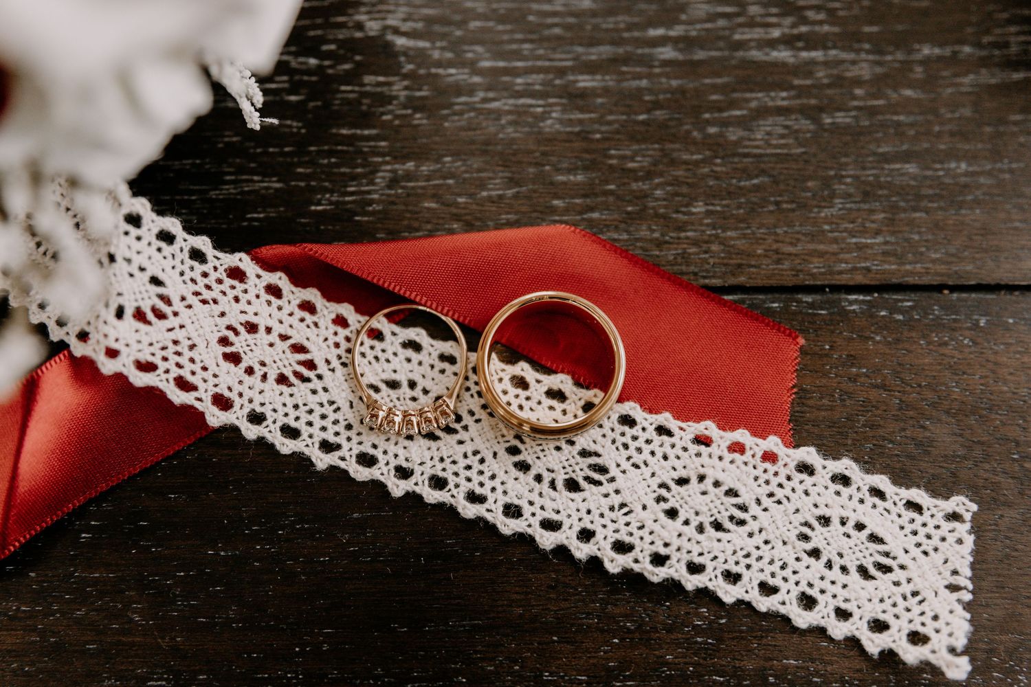 A delicate wedding ring resting on white lace trim and red fabric.