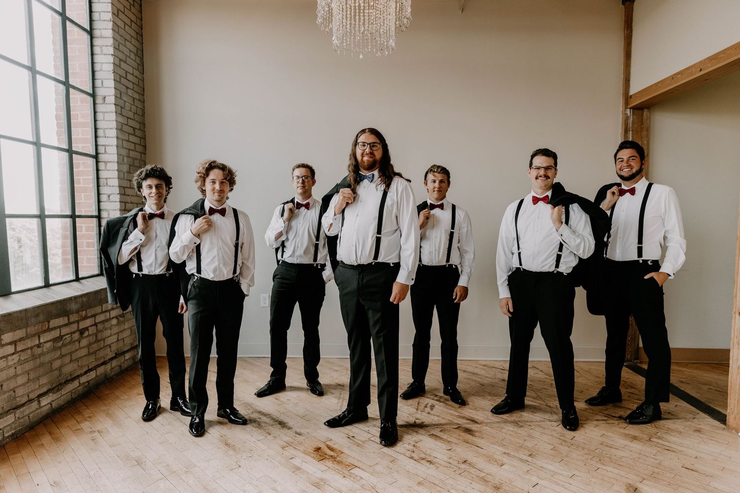 Groomsmen in black suits and suspenders pose together in an industrial wedding venue.