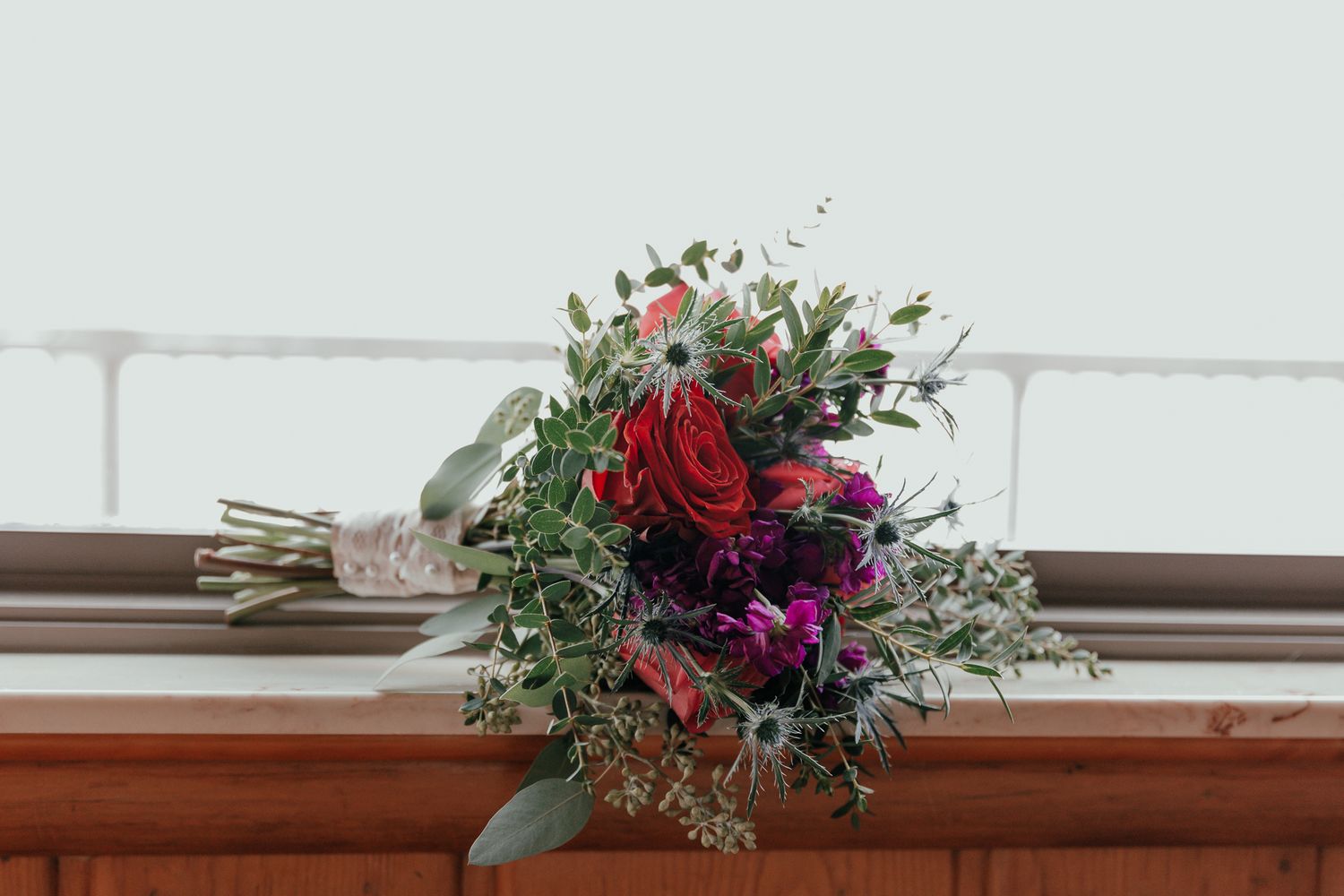 An elegant red and purple wedding bouquet displayed on a wooden surface.