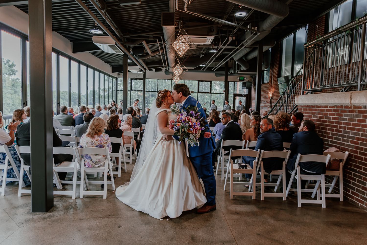 A couple sharing their first dance in an industrial-style venue with exposed beams and brick walls.