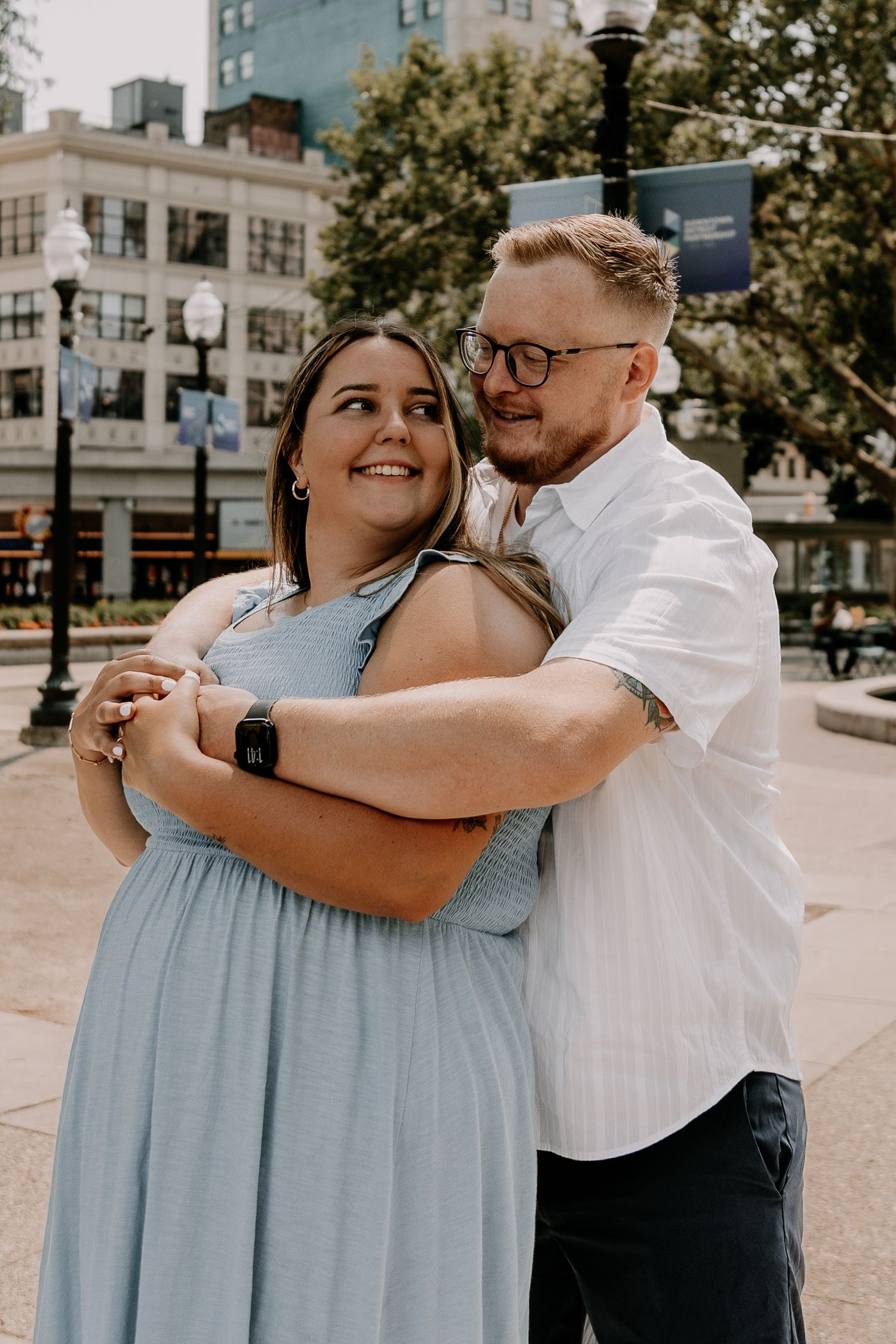 A couple dances together on a city plaza, with her wearing a light blue dress and him in a white button-down shirt.