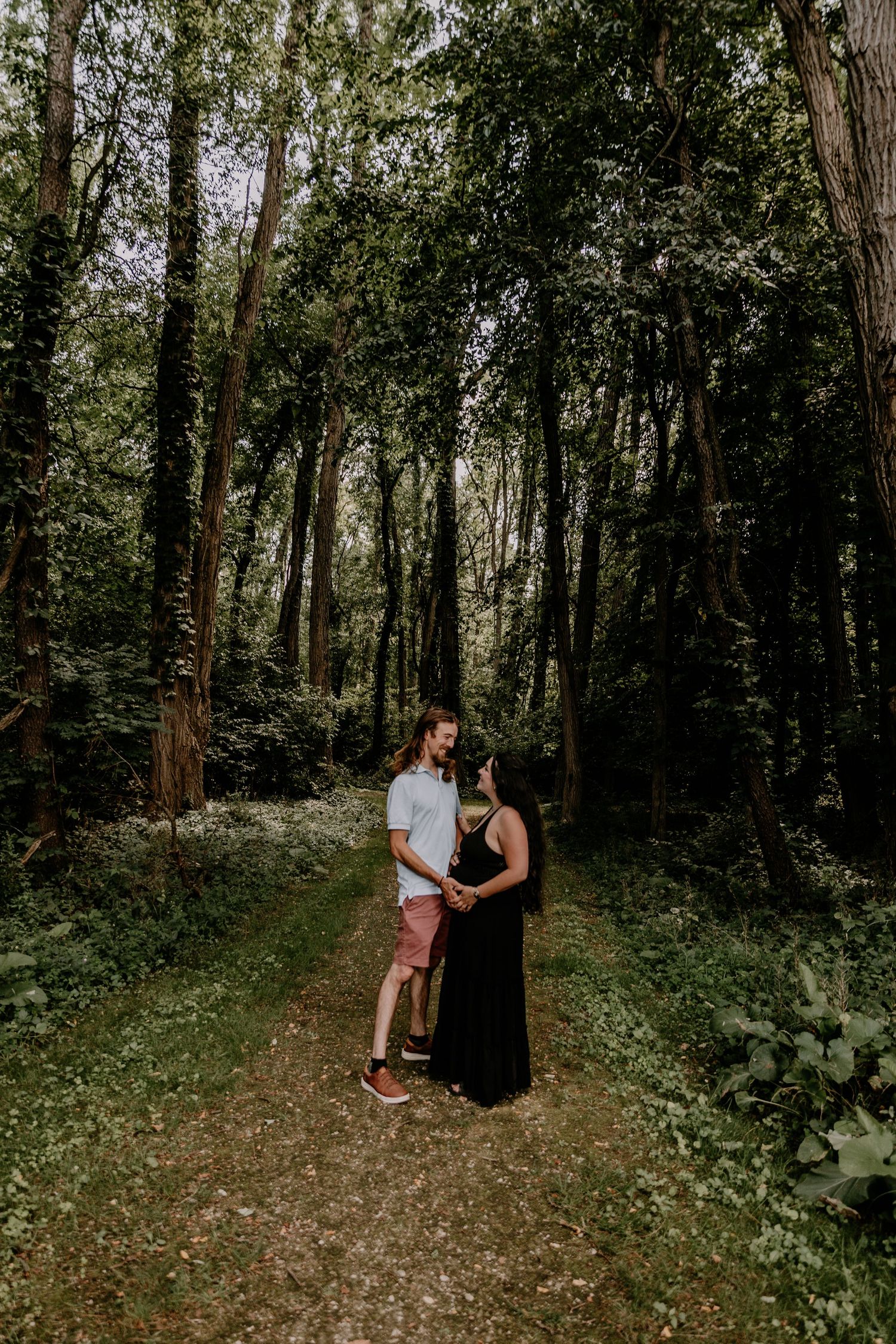 Couple standing together on a forest path surrounded by lush green trees during a maternity photo session.