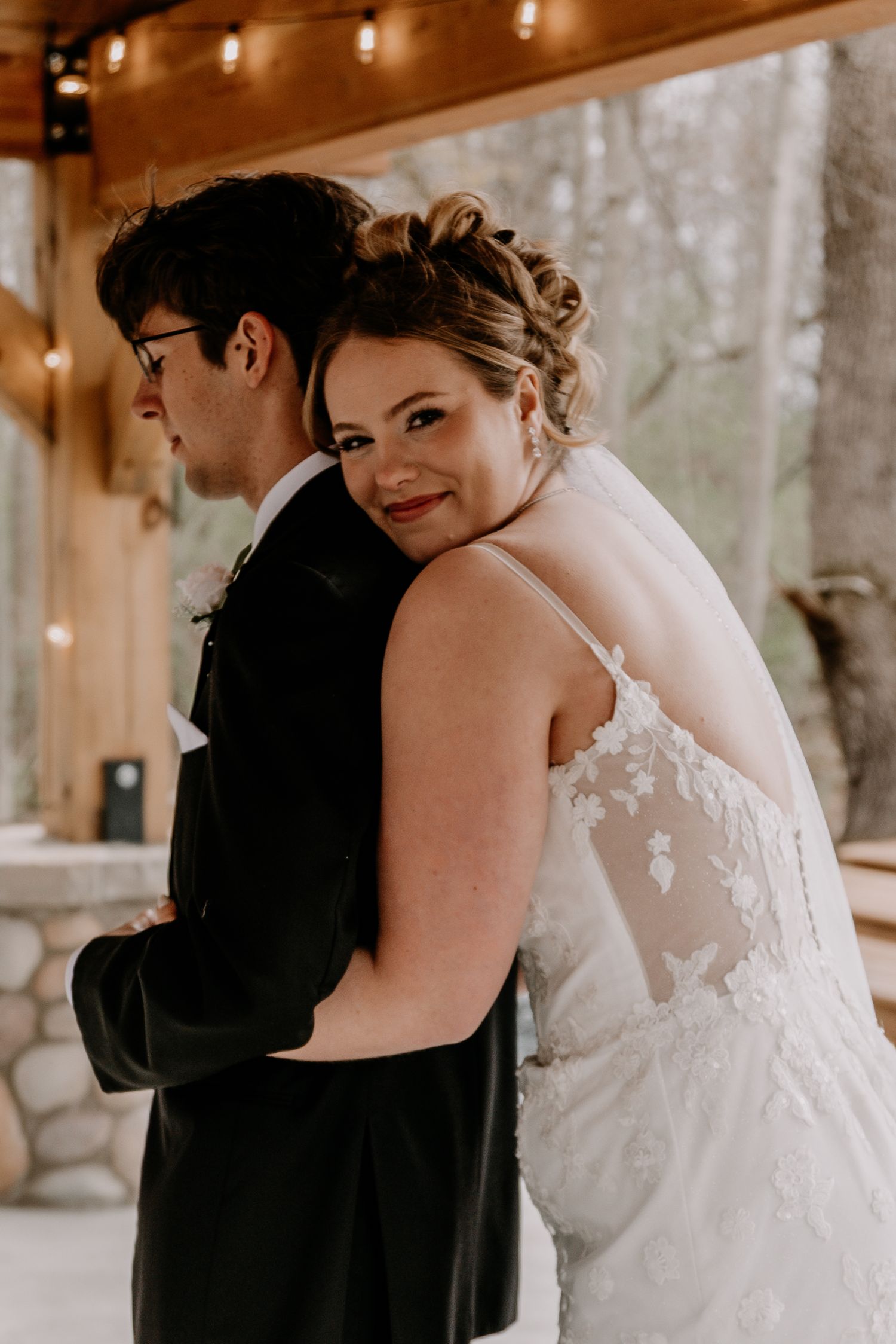 Intimate moment between newlyweds under string lights in wooden venue.
