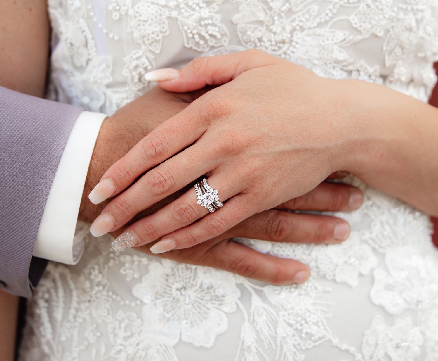 Close-up of newlyweds' hands showing diamond engagement ring and wedding bands.
