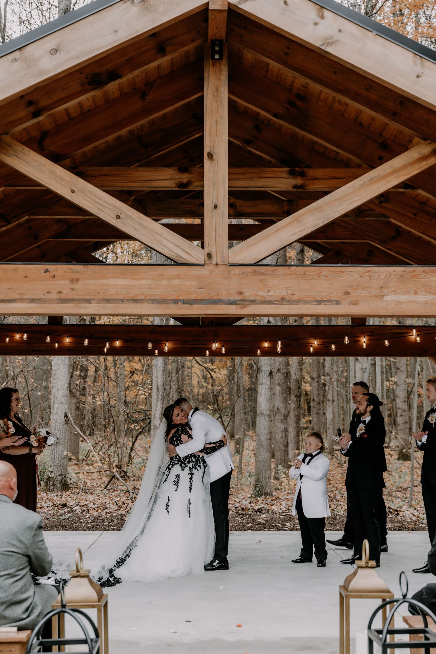 Rustic barn wedding ceremony with wooden beams and string lights in a birch forest setting.