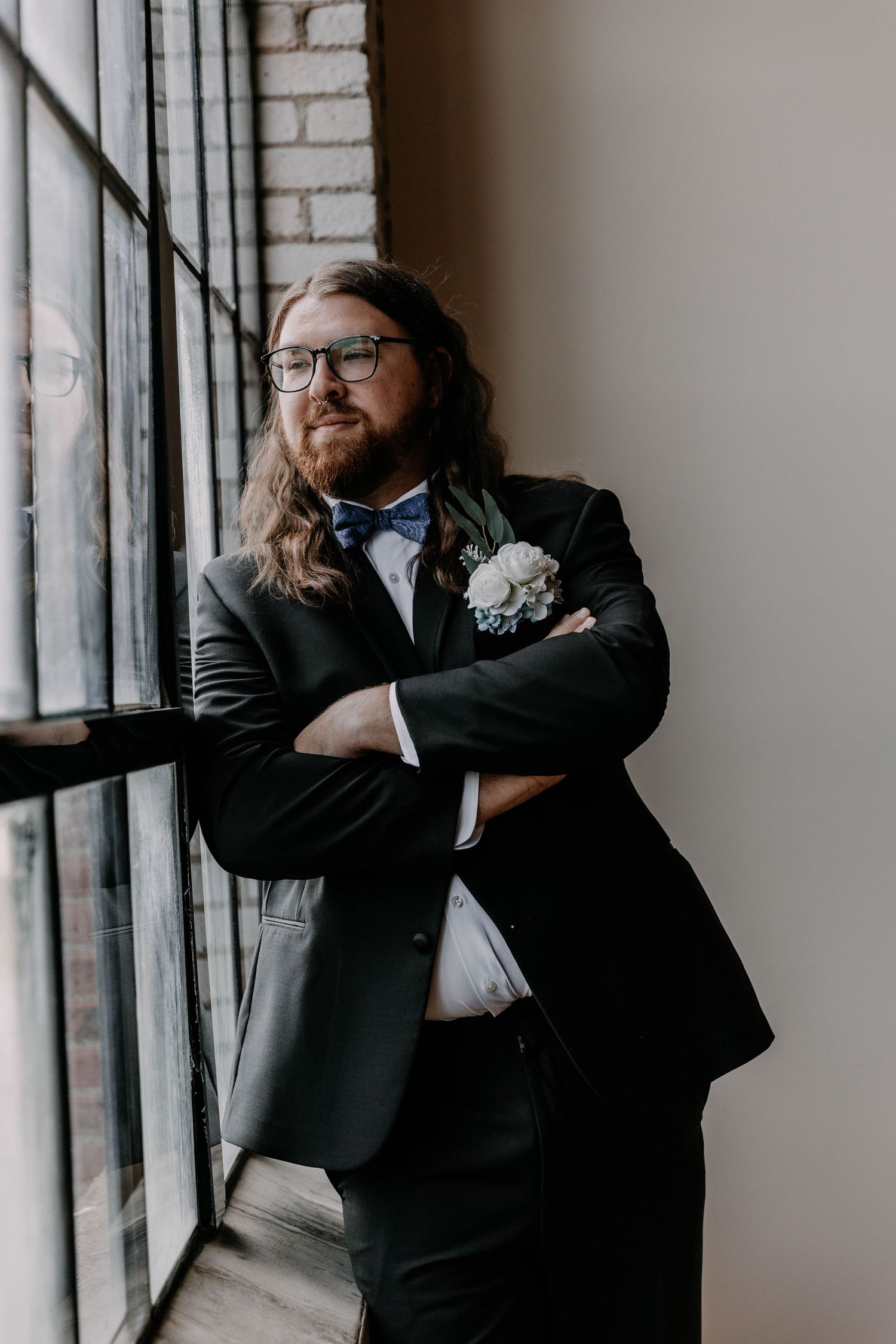 A person in glasses and formal attire gazes thoughtfully out large industrial windows.