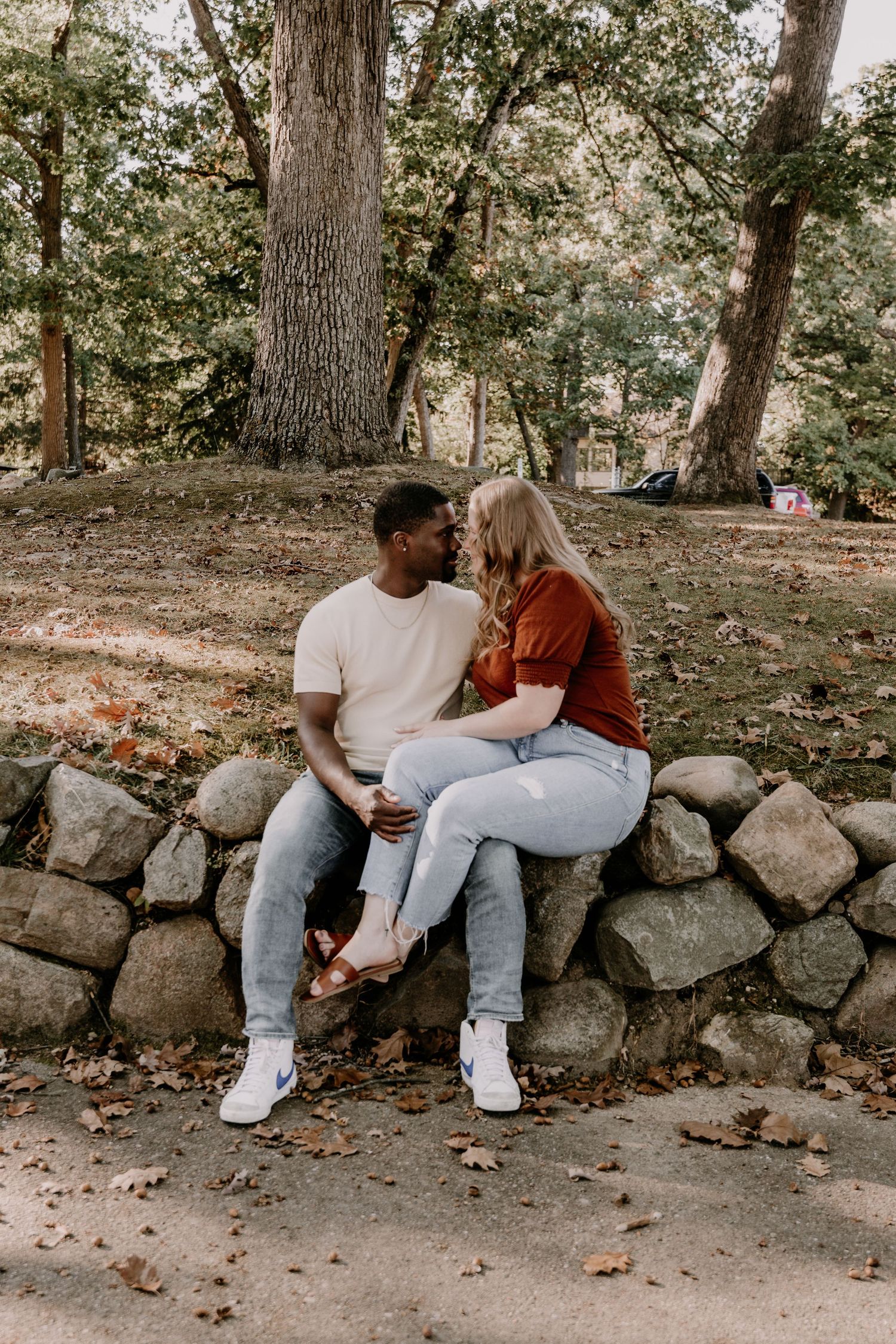 A couple sits together on a stone wall in a wooded area, shown in a progressive sequence of three intimate moments.