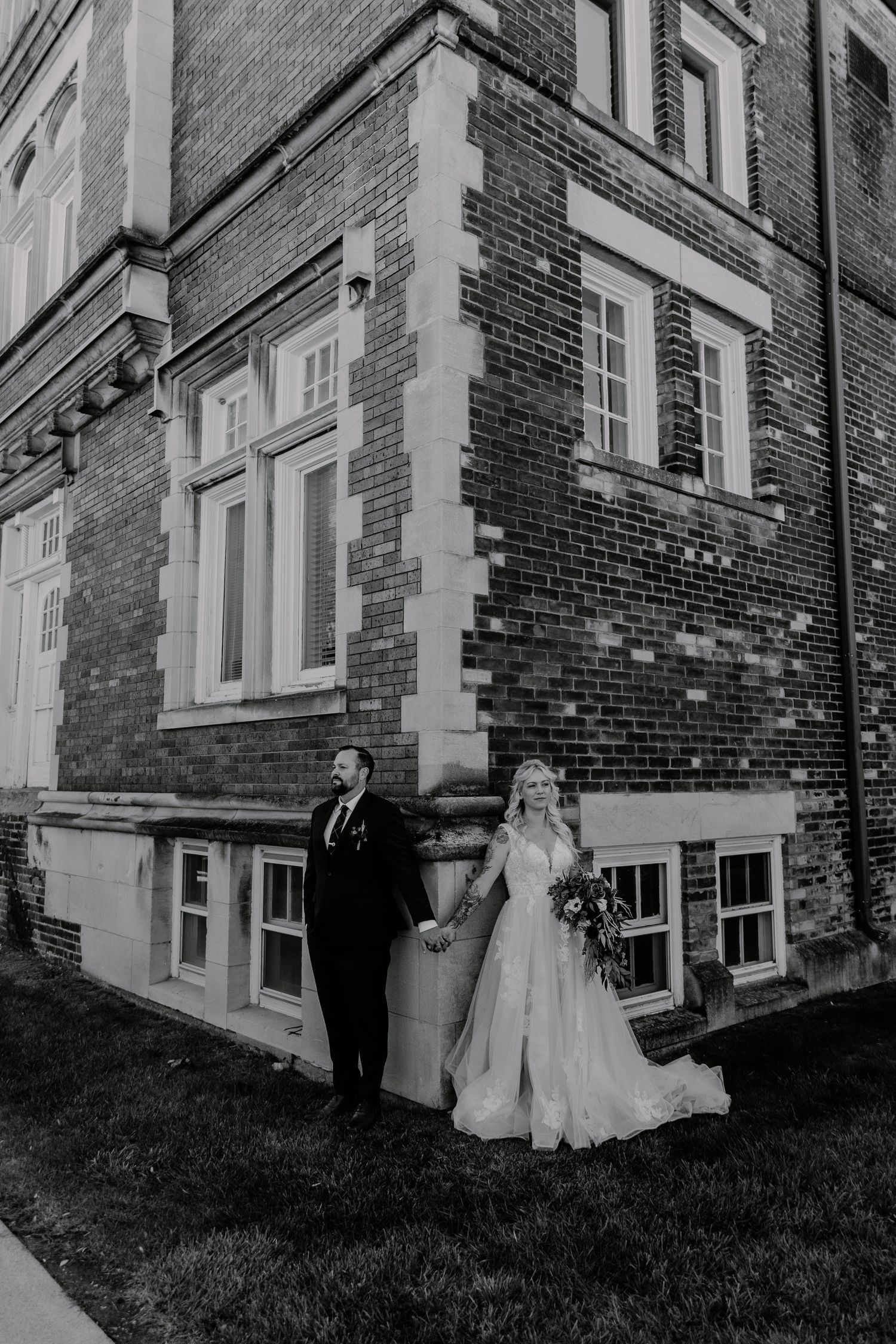 A black and white wedding photo against a historic brick building with white trim windows.