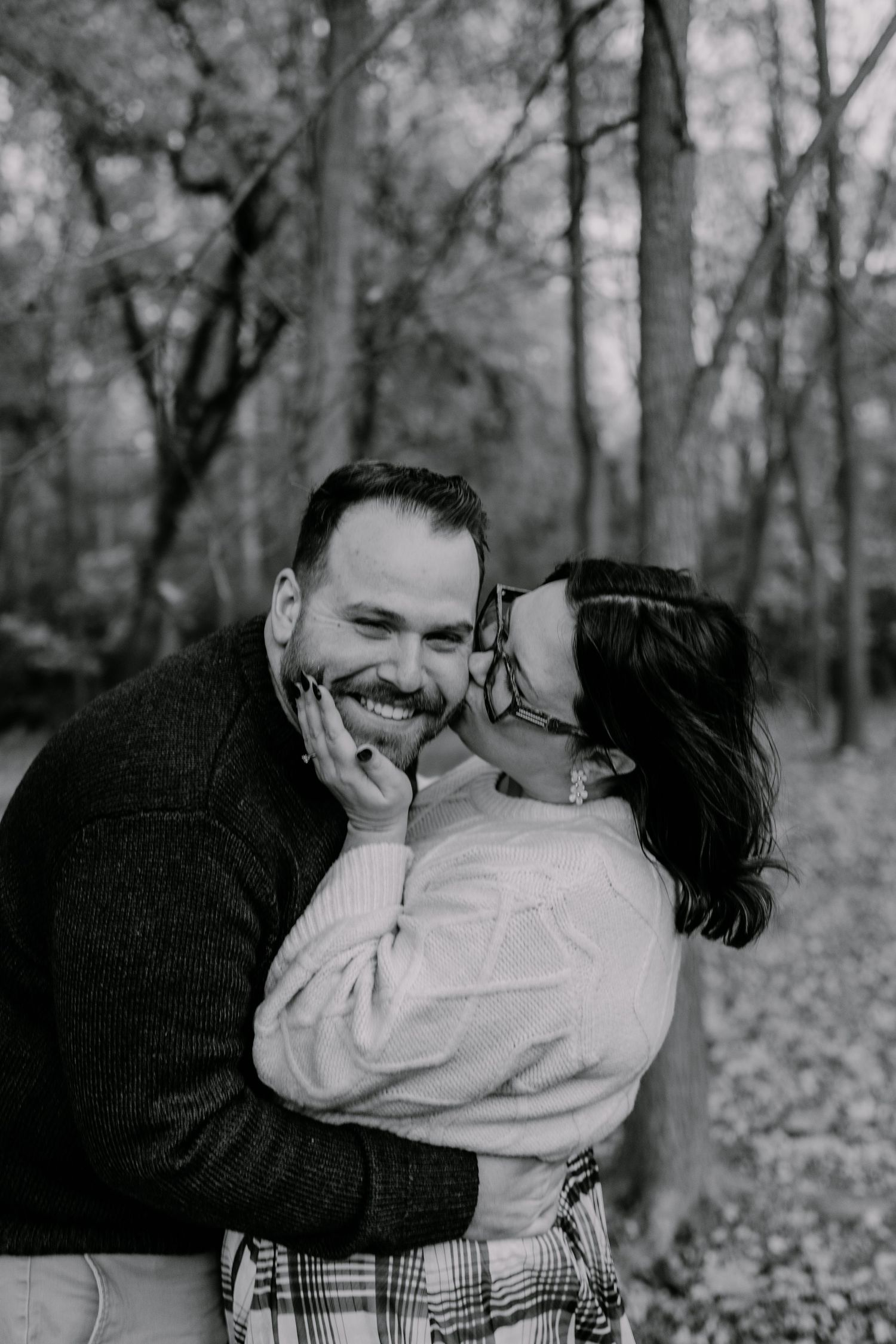 A romantic black and white photo series of a couple embracing and laughing together in a wooded autumn setting.