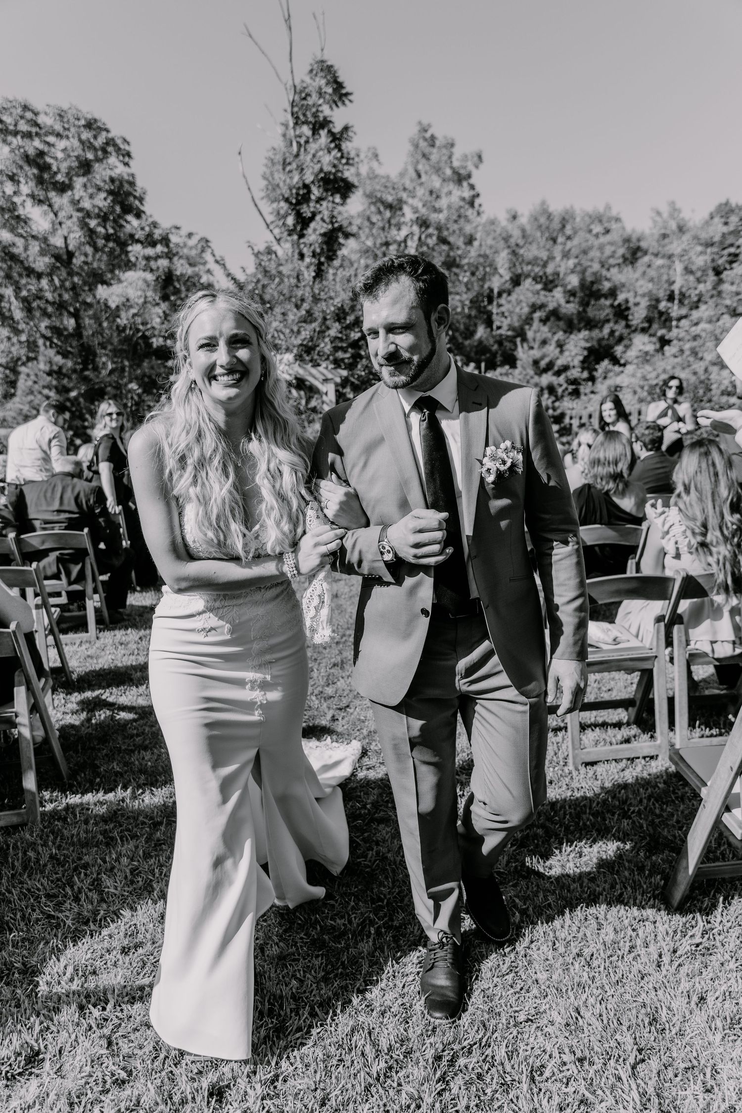 A joyful wedding ceremony exit with a couple walking down an outdoor aisle lined with chairs.