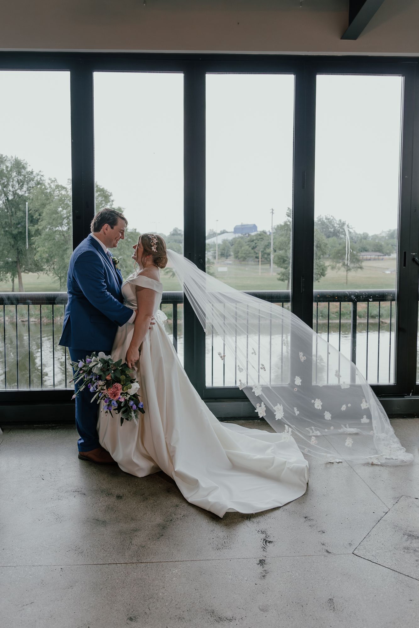 Wedding couple in elegant attire share romantic moments in a modern venue with large windows.