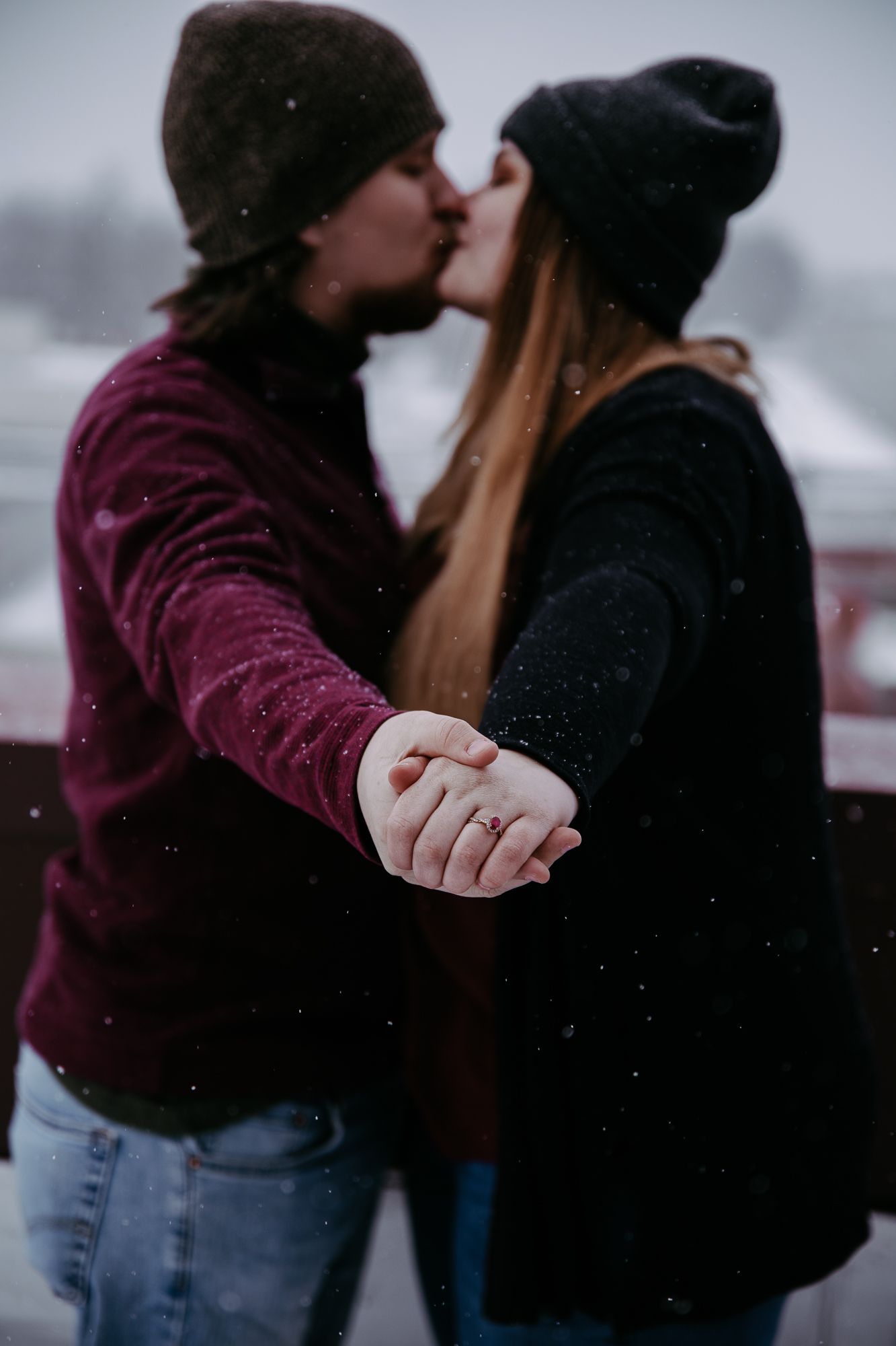 A couple sharing an intimate embrace in winter, dressed in burgundy and black outerwear.