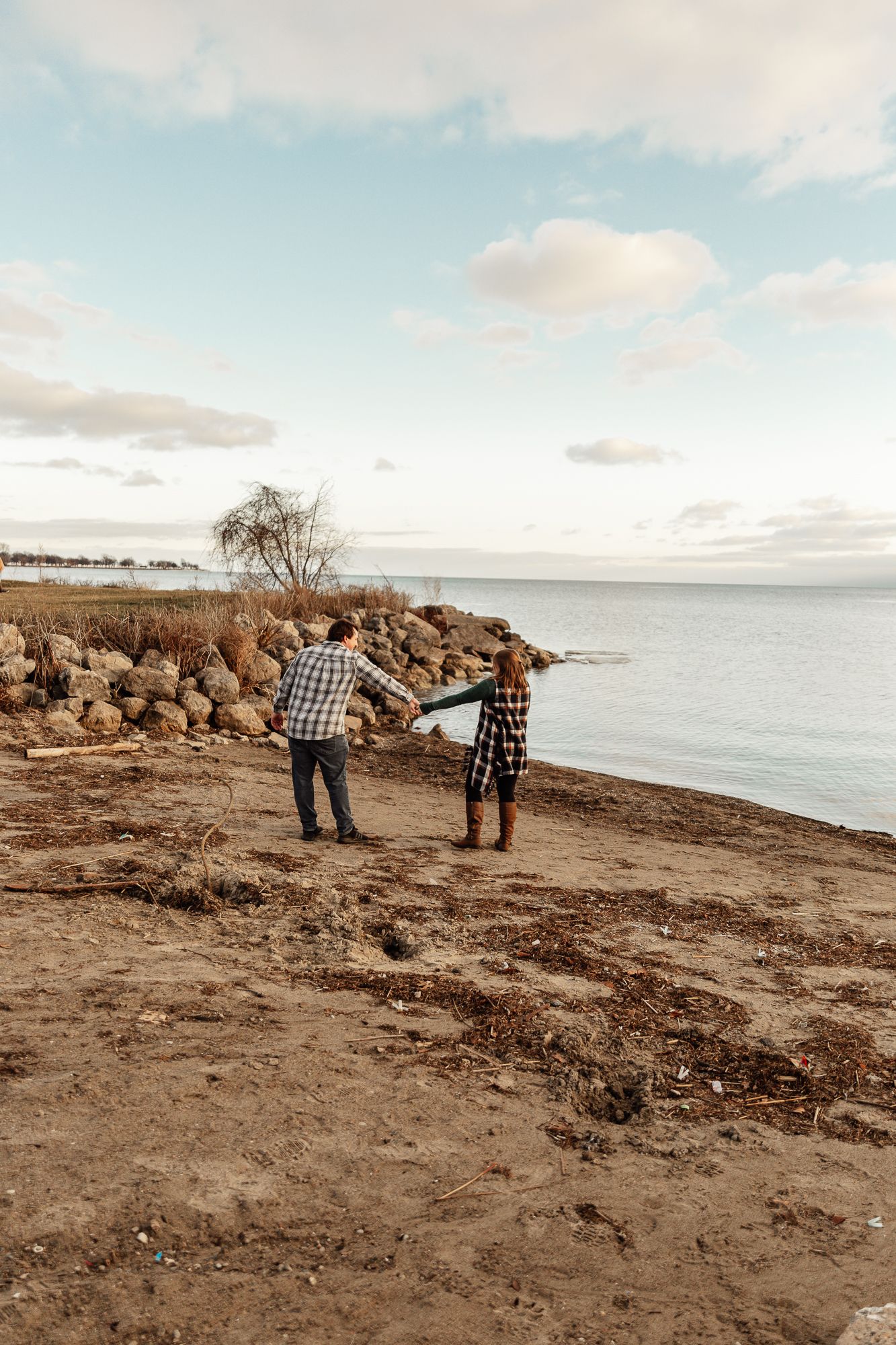 A couple holding hands while walking along a coastal cliff at sunset.