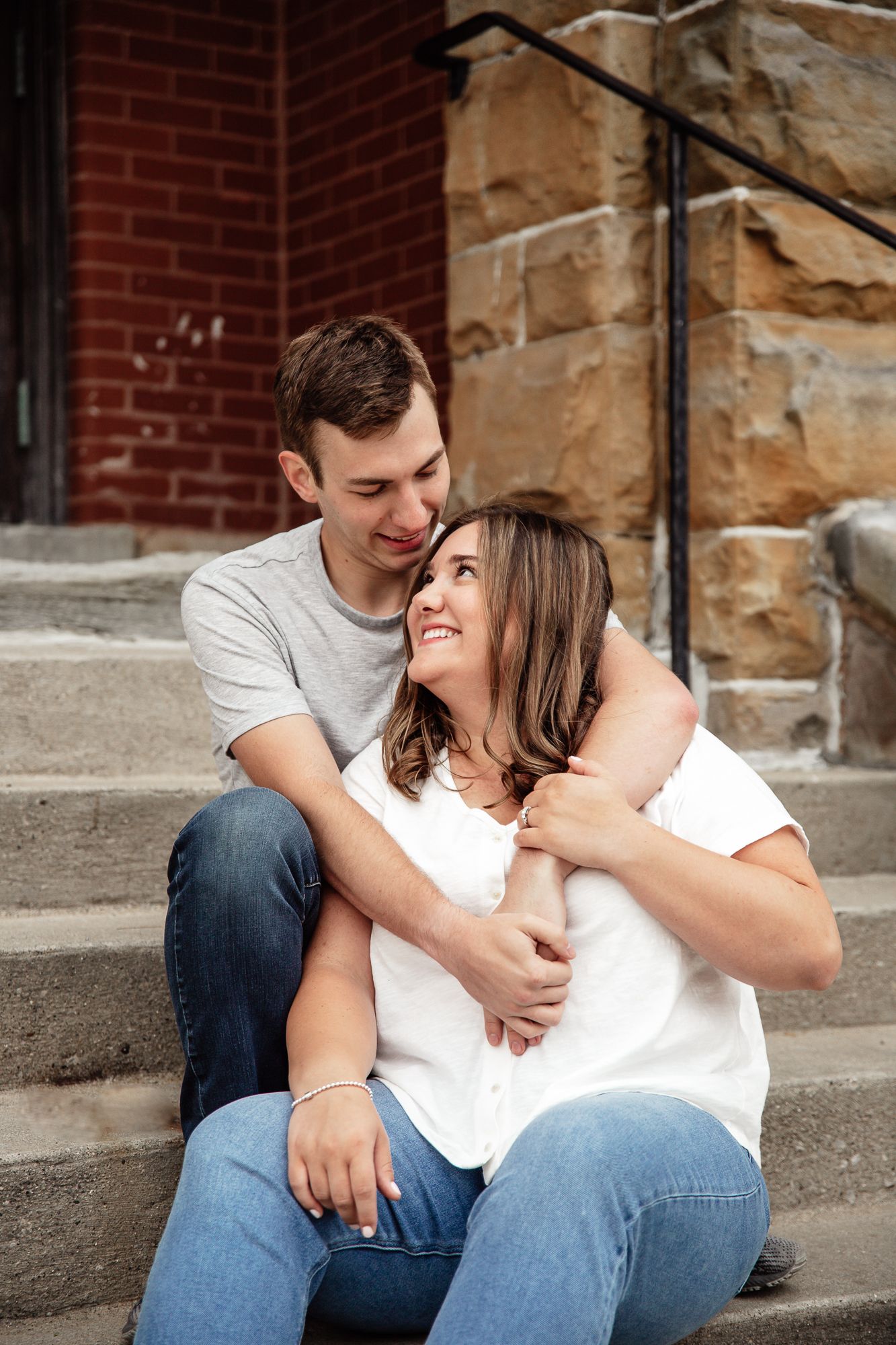 Couple shares intimate moment while sitting on stone steps during engagement shoot.