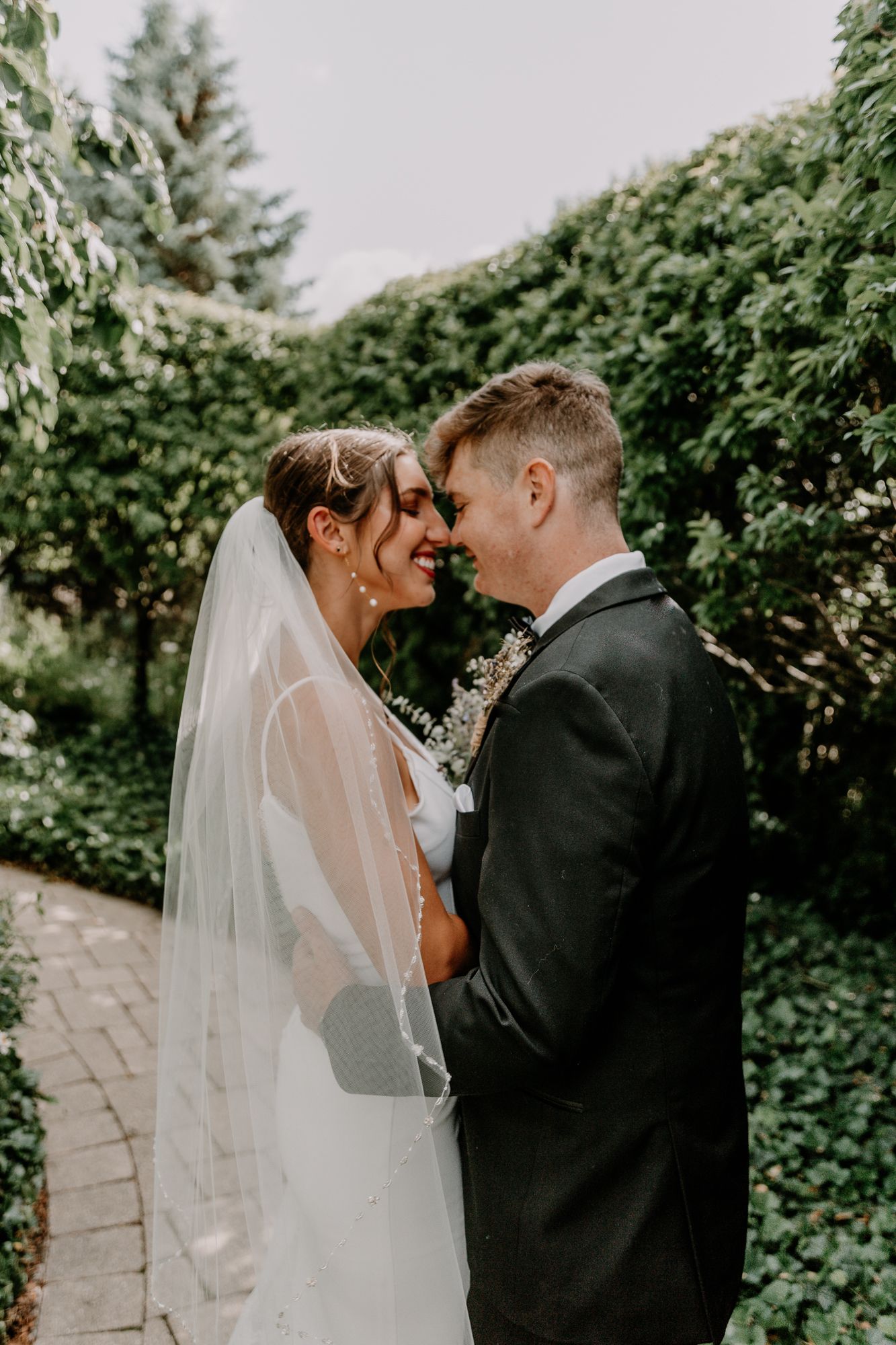 Intimate moment between couple on garden path with flowing veil.
