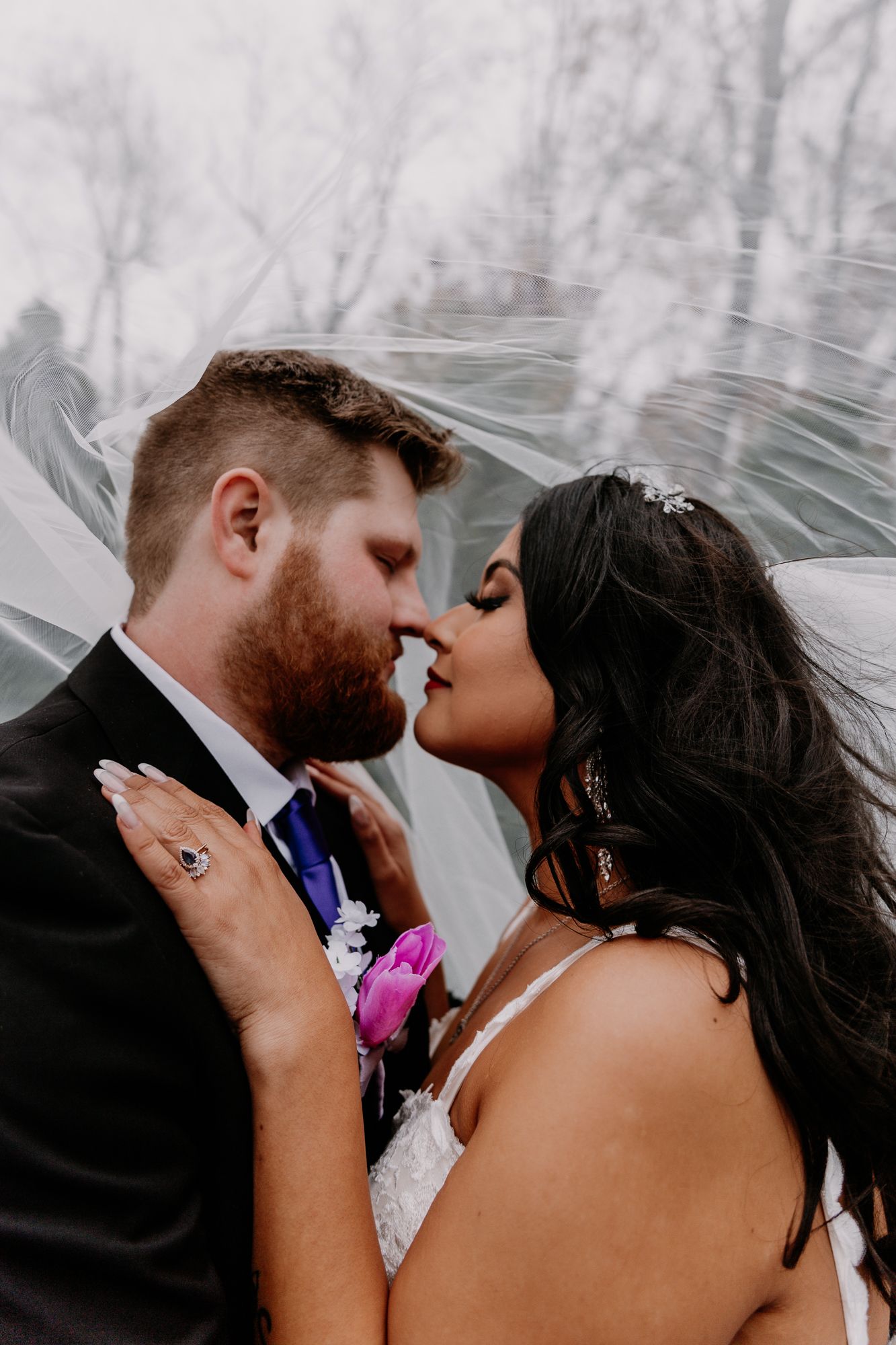 Close-up of bride and groom sharing romantic moment with pink boutonniere and flowing veil.