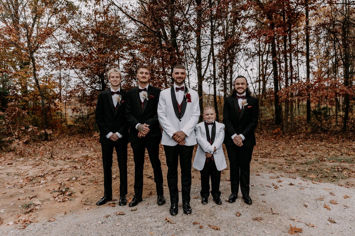 Wedding party in formal black and white attire posed together in autumn woodland setting.