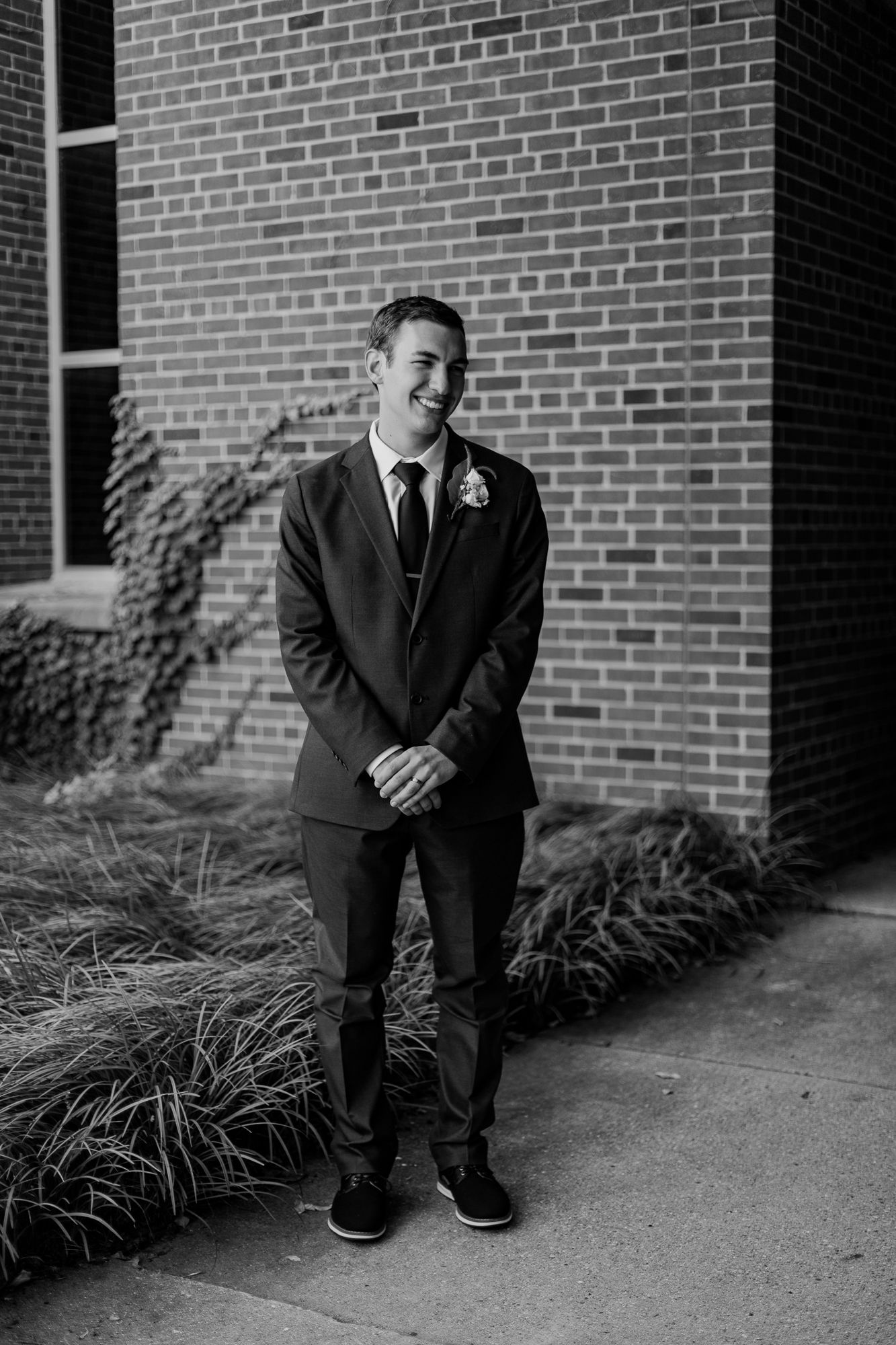 Black and white portrait of groom in classic suit standing against brick wall.