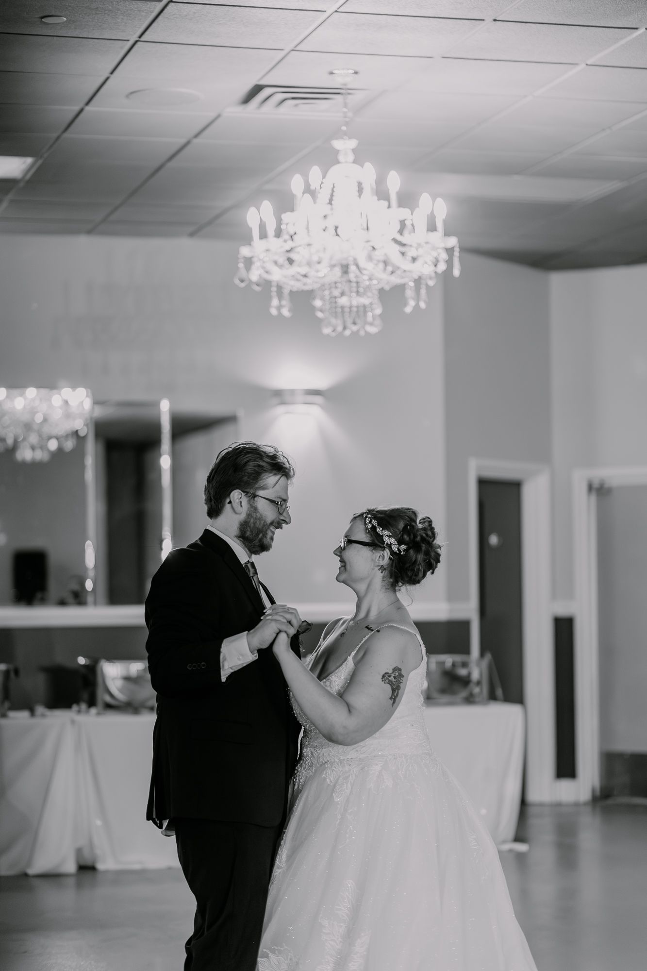 Couple shares their first dance in an elegant ballroom under crystal chandeliers.