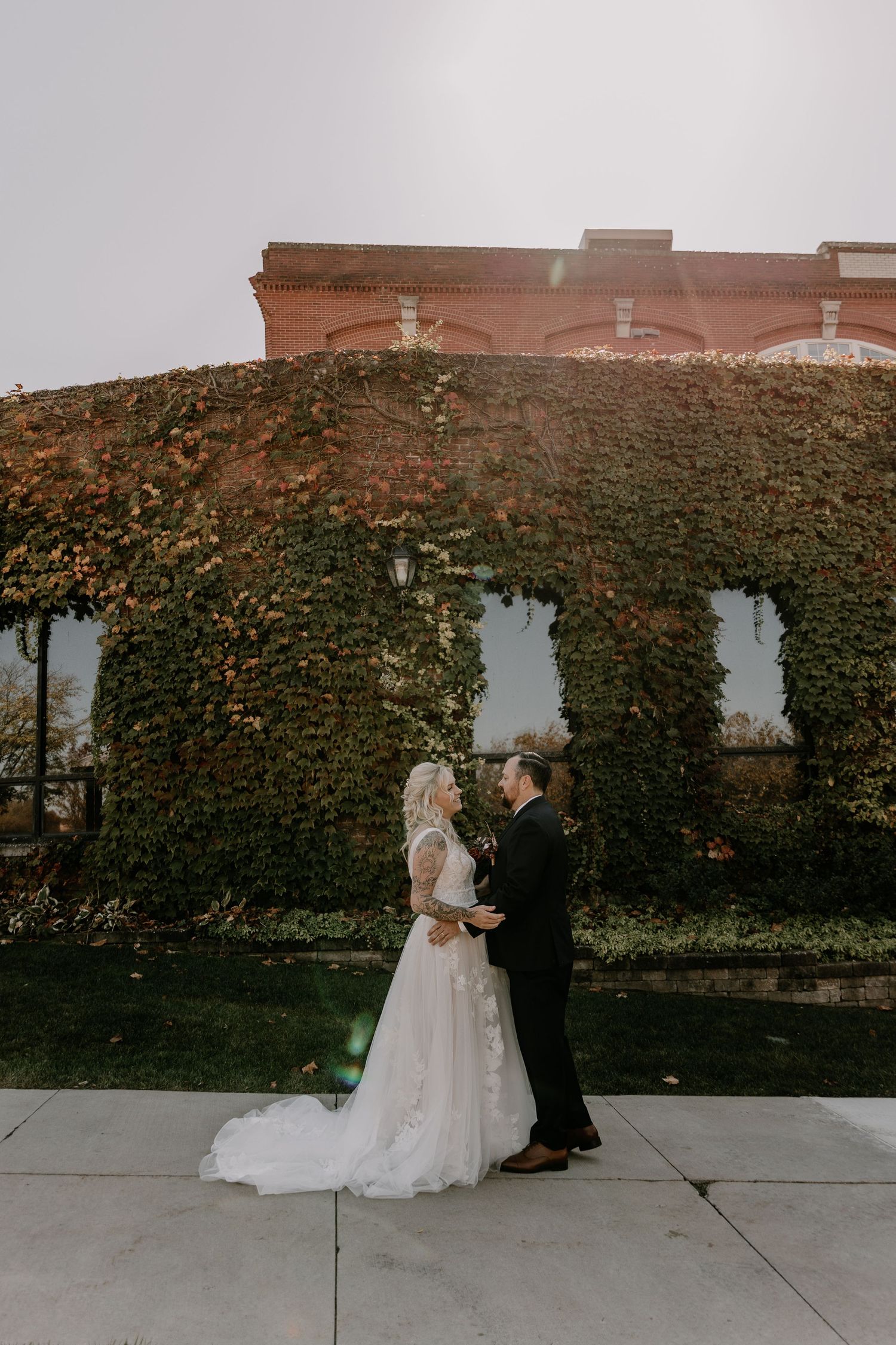 A couple shares an intimate moment against an ivy-covered brick wall during their wedding photoshoot.