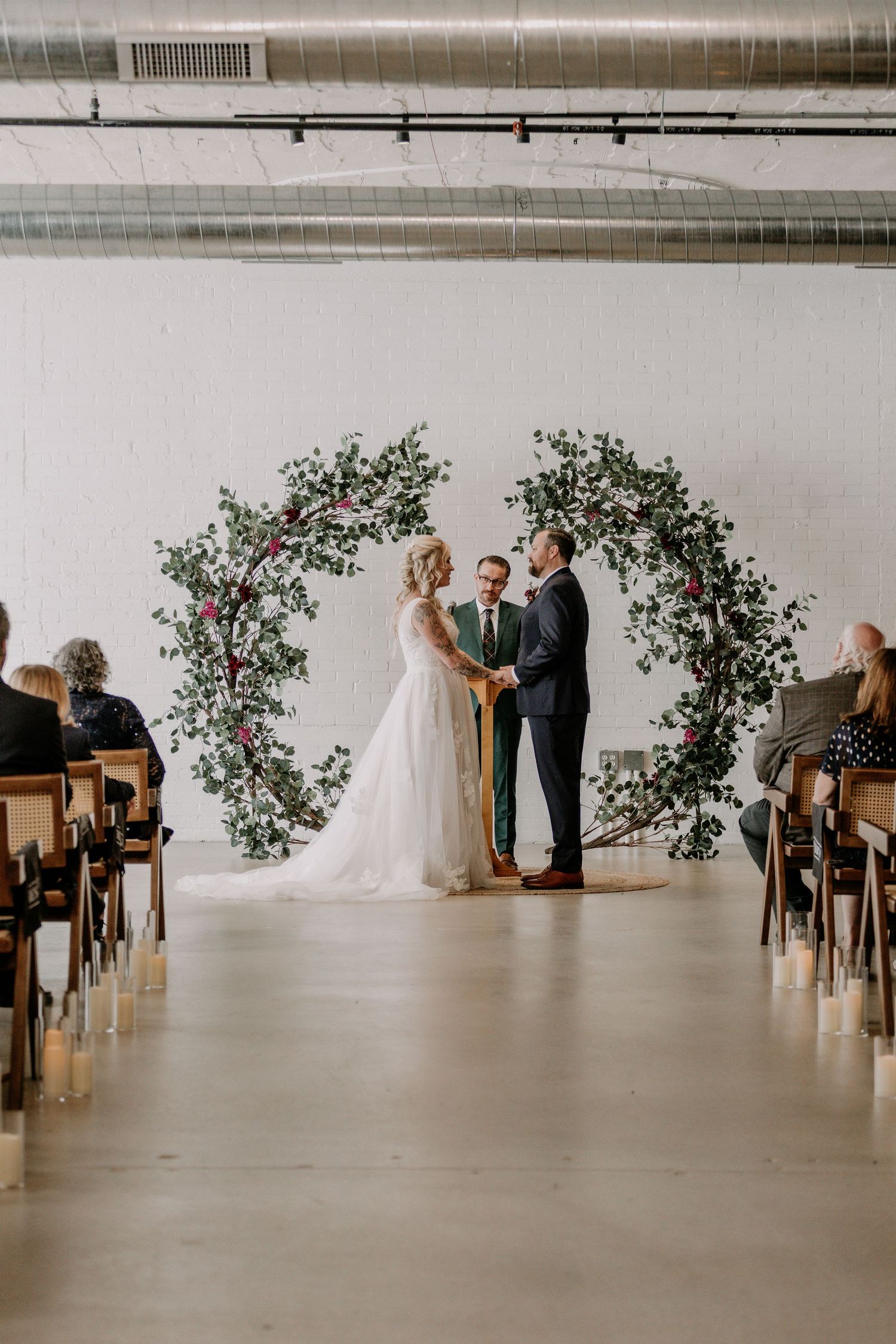 An elegant wedding ceremony setup with floral arches and wooden chairs in a minimalist white space.
