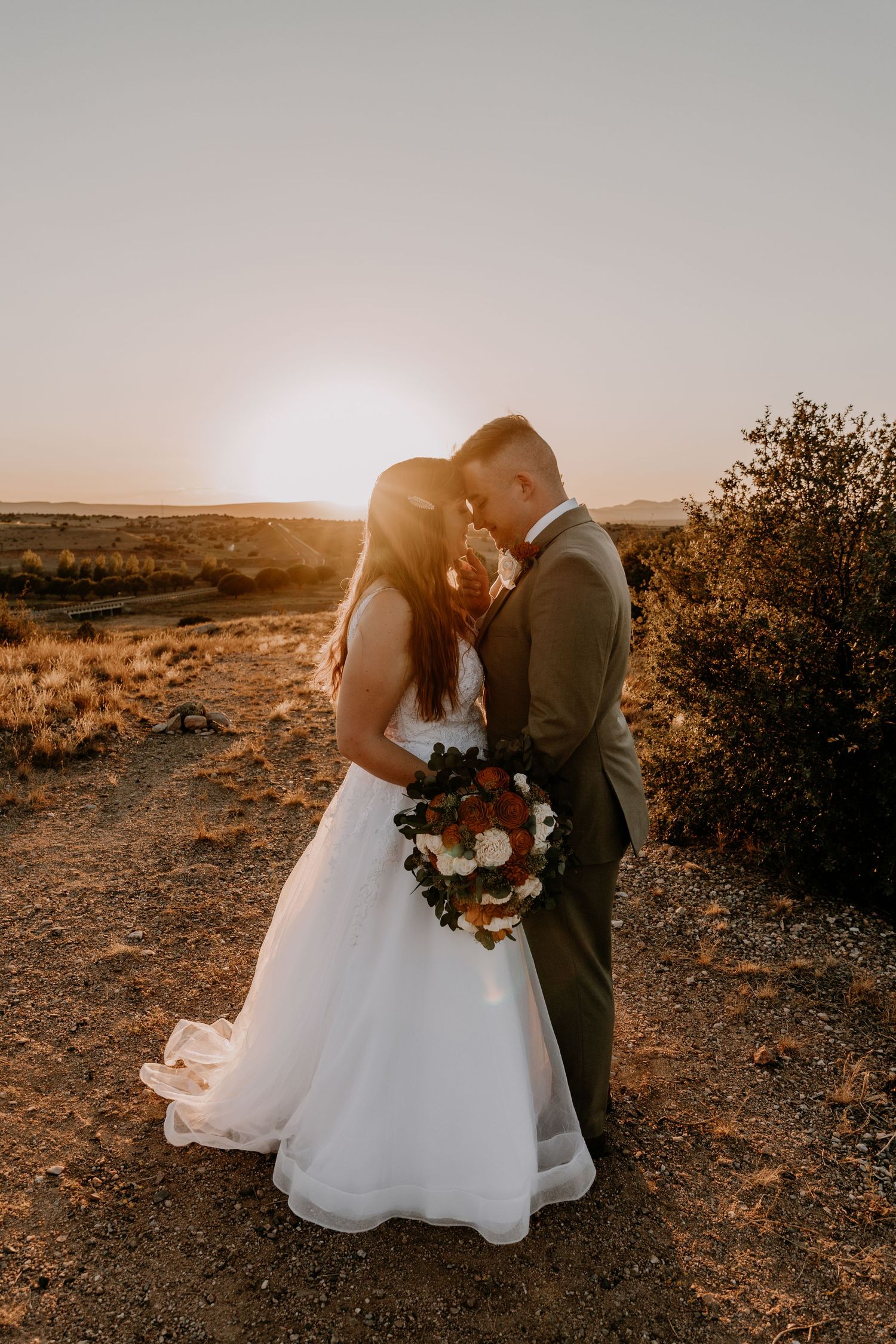 A romantic desert wedding shoot with soft sunlight illuminating the couple against the rugged terrain.