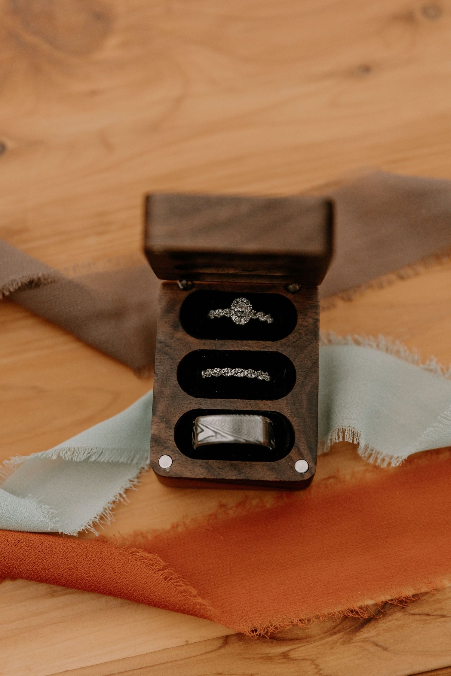 Three wedding rings displayed in wooden box on fabric background.