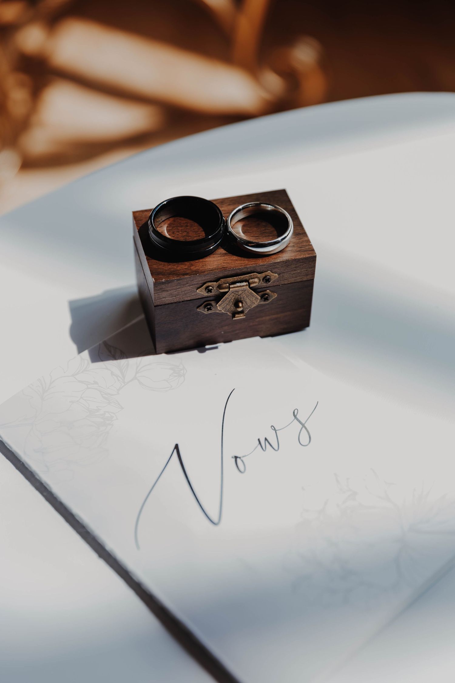 Wooden ring box and handwritten vows on white surface in natural light.