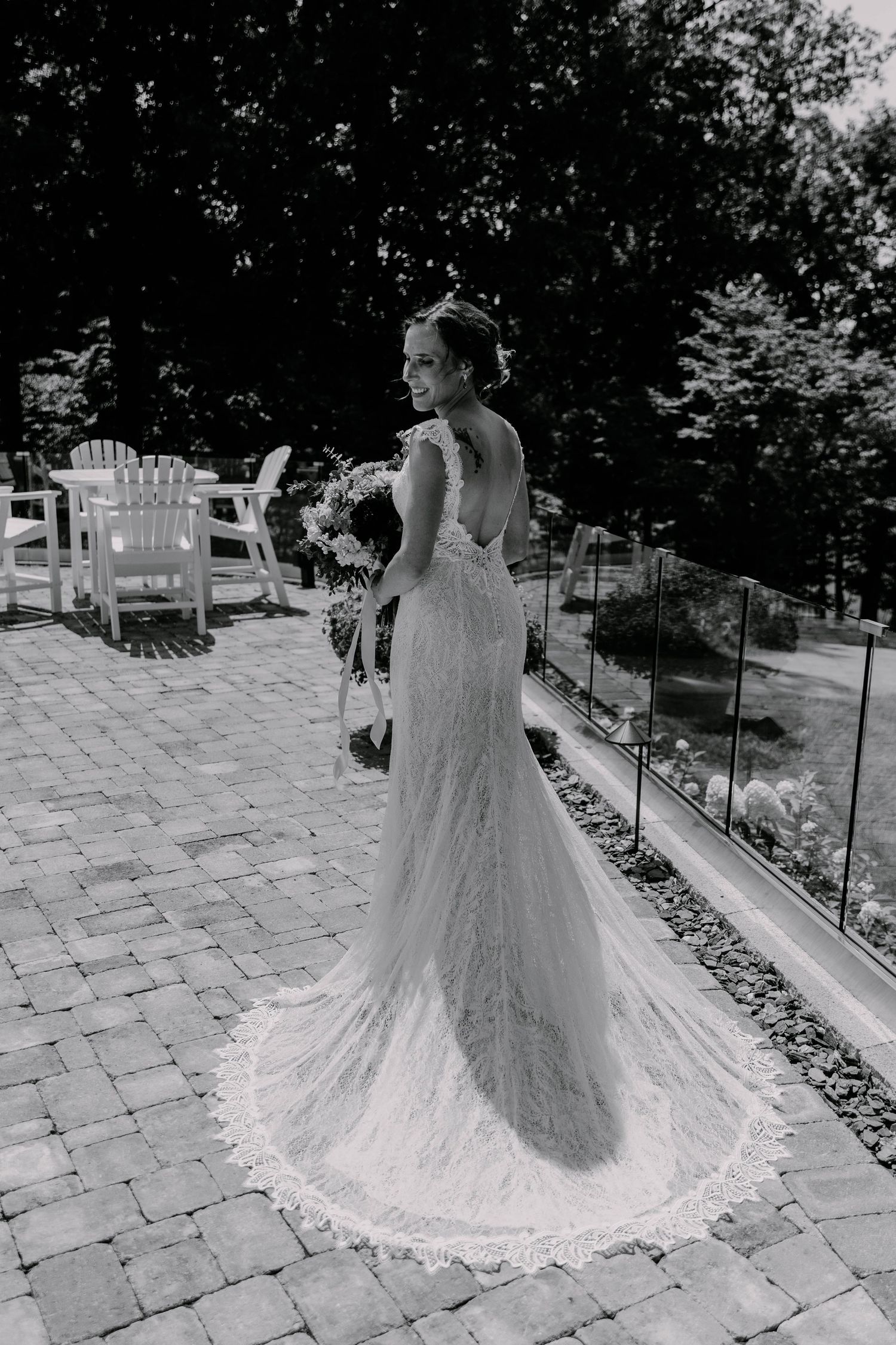 A black and white photo capturing a bride's lace train on an outdoor stone patio.