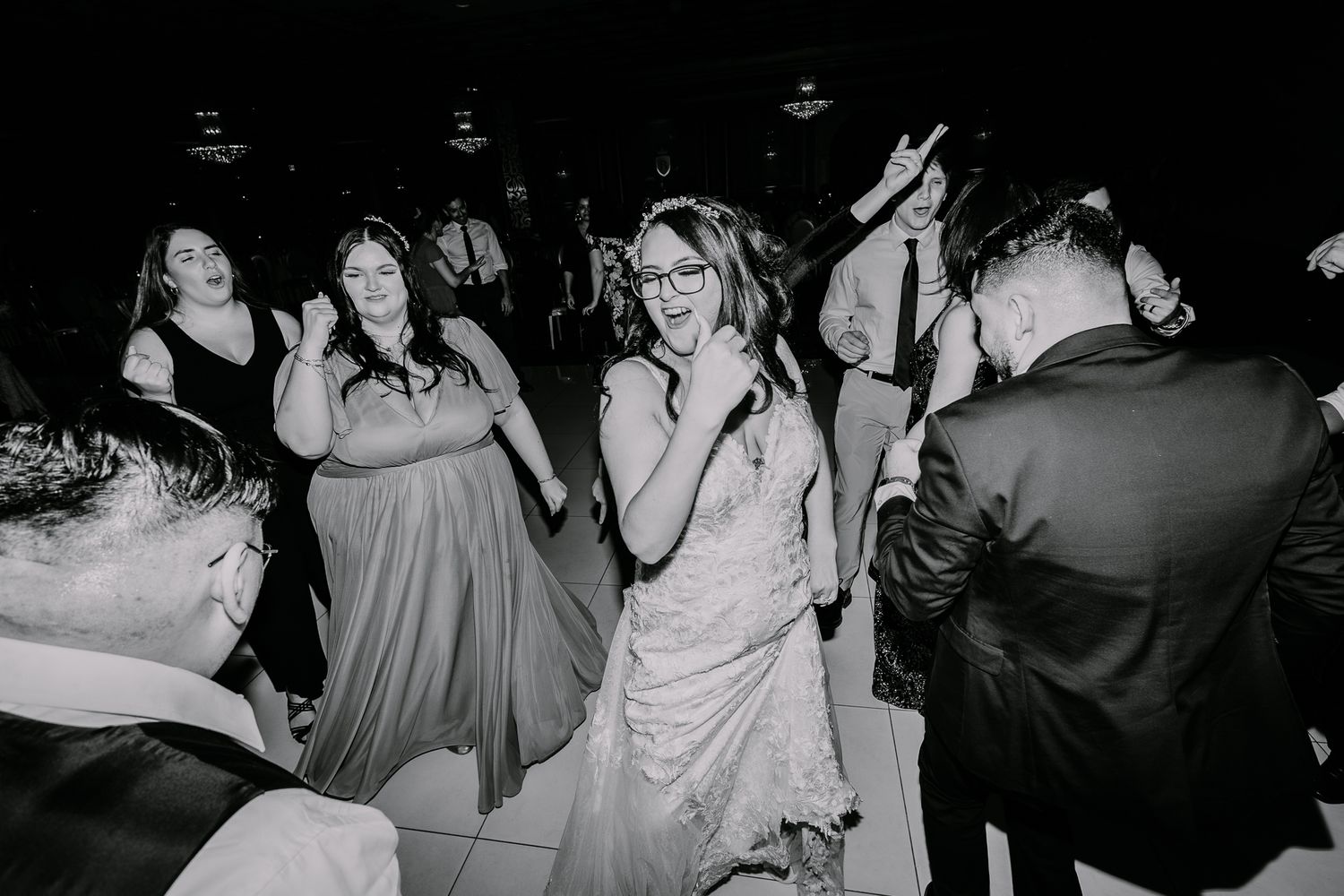 Black and white photo of wedding guests dancing and celebrating on the reception dance floor.