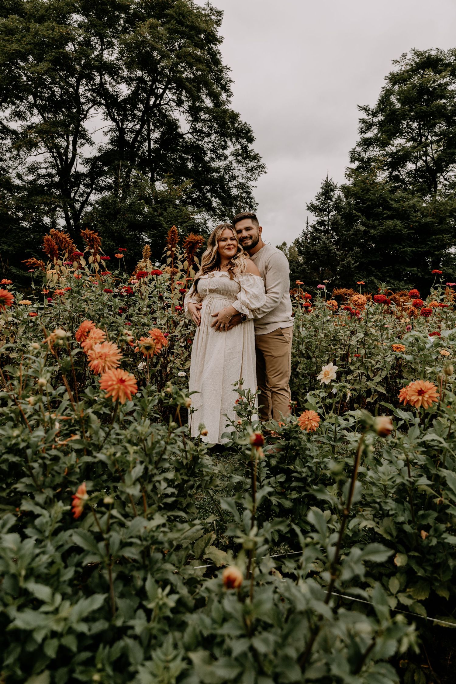 Romantic garden photoshoot among tall orange dahlias and lush greenery.