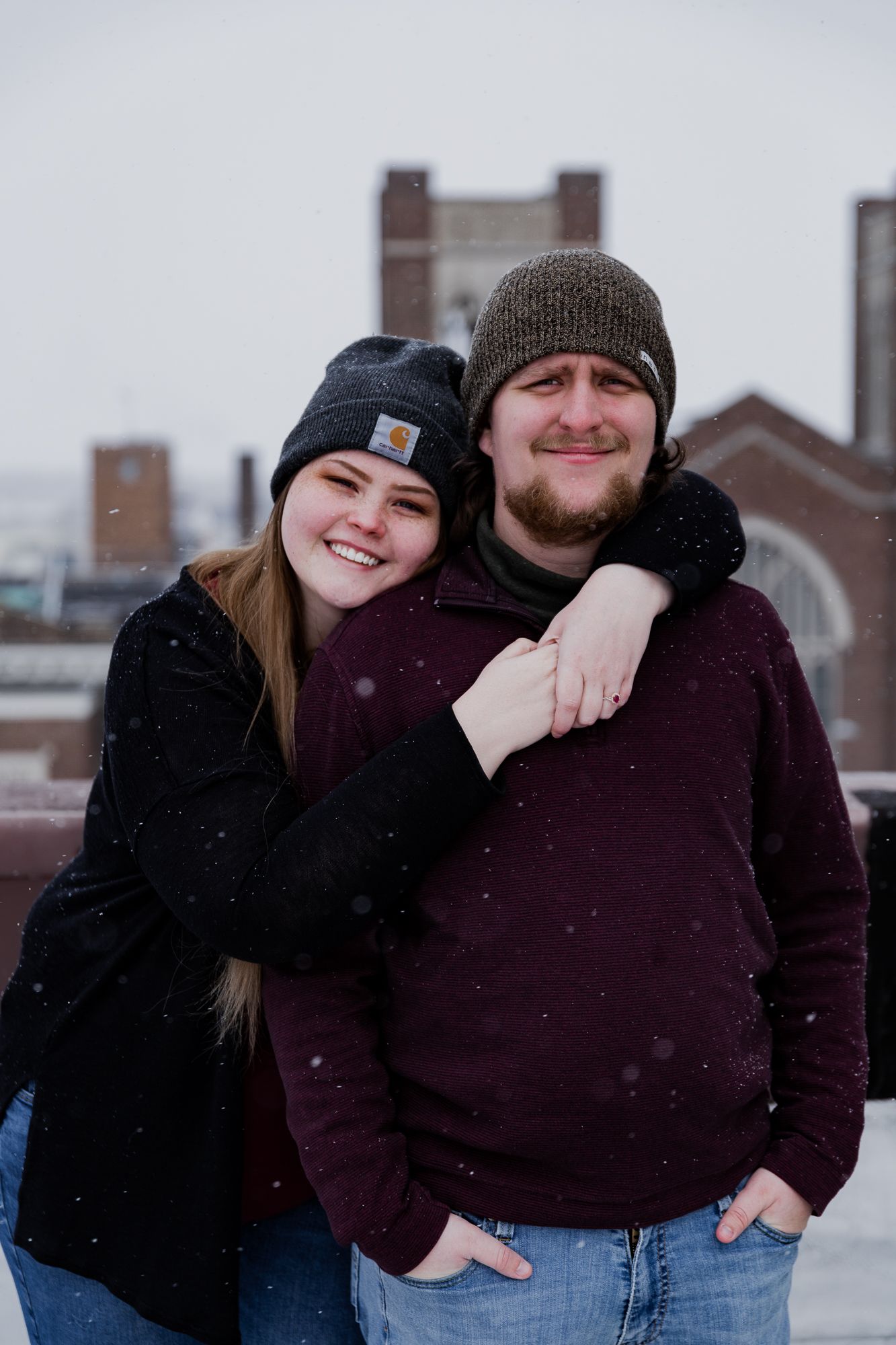 A couple sharing affectionate moments in winter wear against a snowy backdrop.