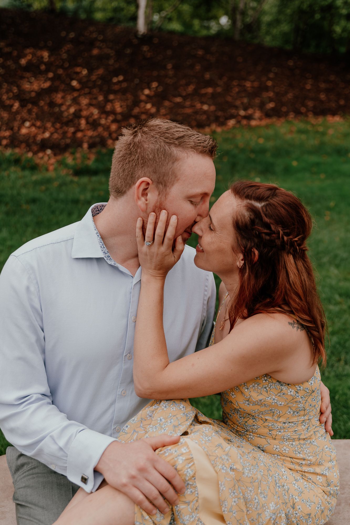 An engaged couple shares a tender moment while sitting together outdoors.