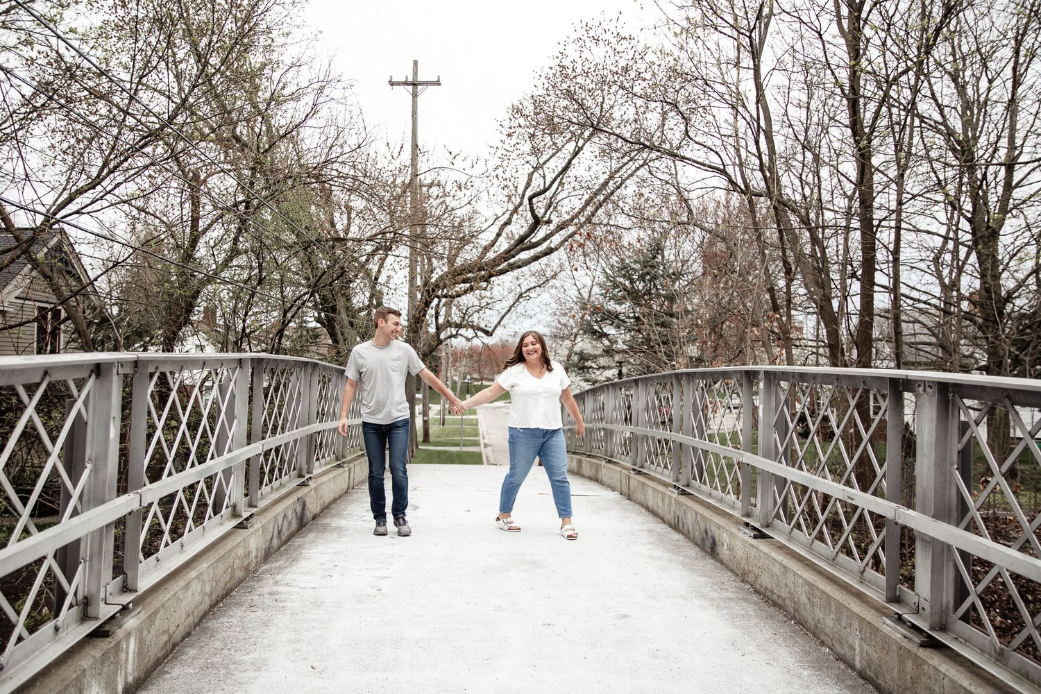 Couple playfully poses on snow-covered bridge during winter engagement session.