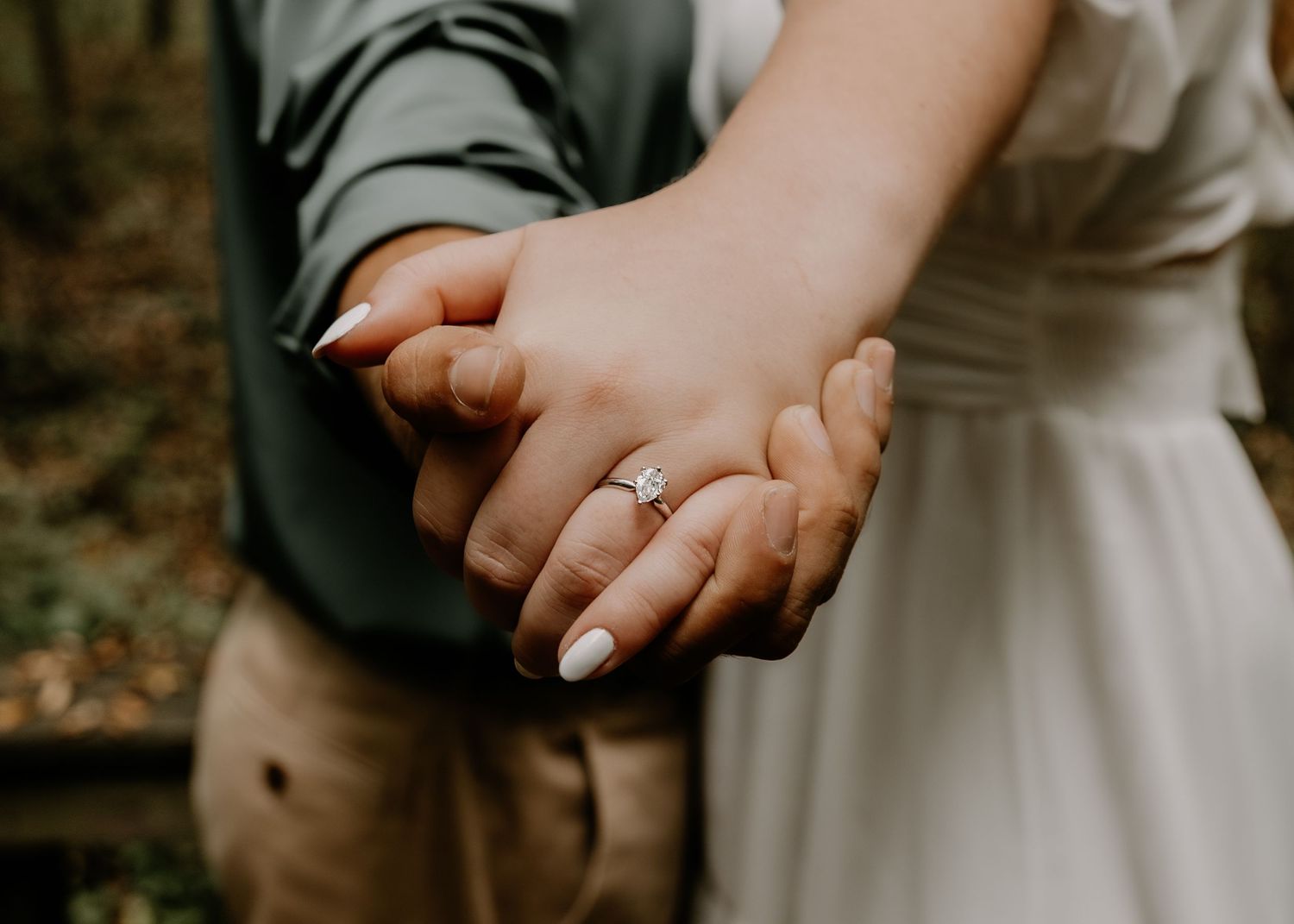 Intimate engagement photo of couple's hands with ring in natural outdoor setting.