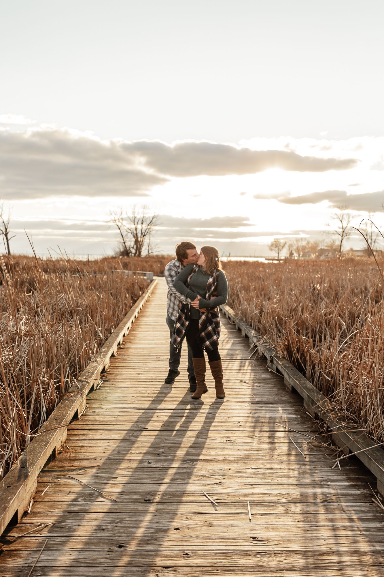A couple embracing on a wooden boardwalk during golden hour.