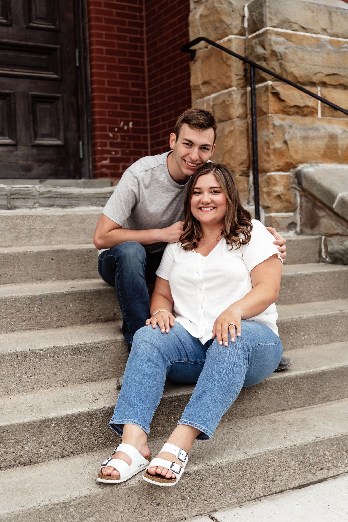 Couple poses together on stone church steps during engagement photo session.