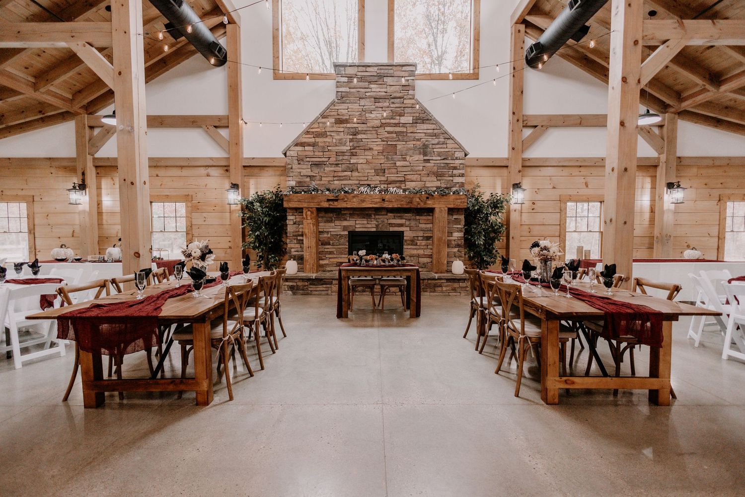 Rustic barn wedding reception setup with long wooden tables and stone fireplace focal point.