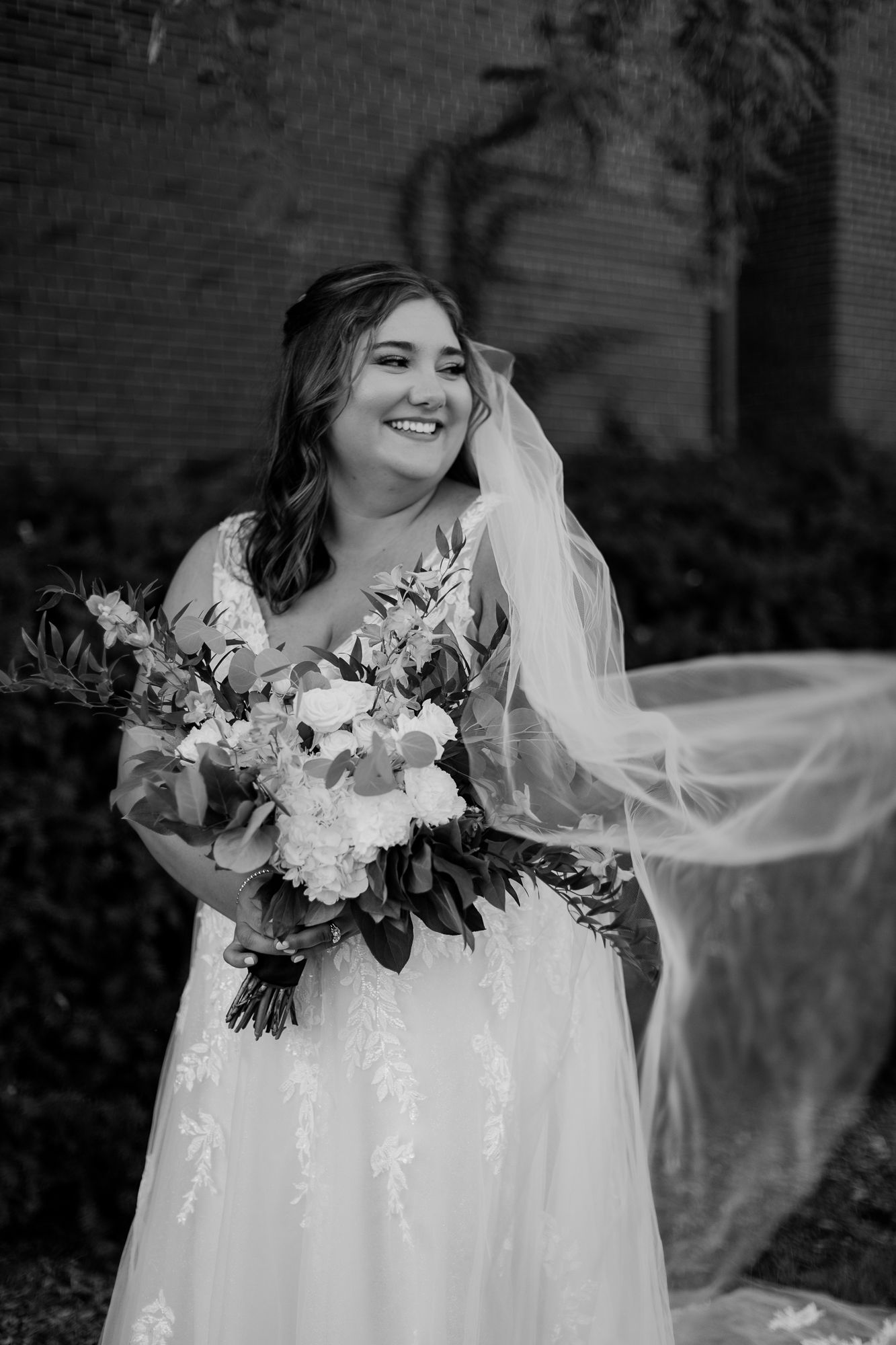 Black and white portrait of bride holding bouquet with flowing veil in the wind.