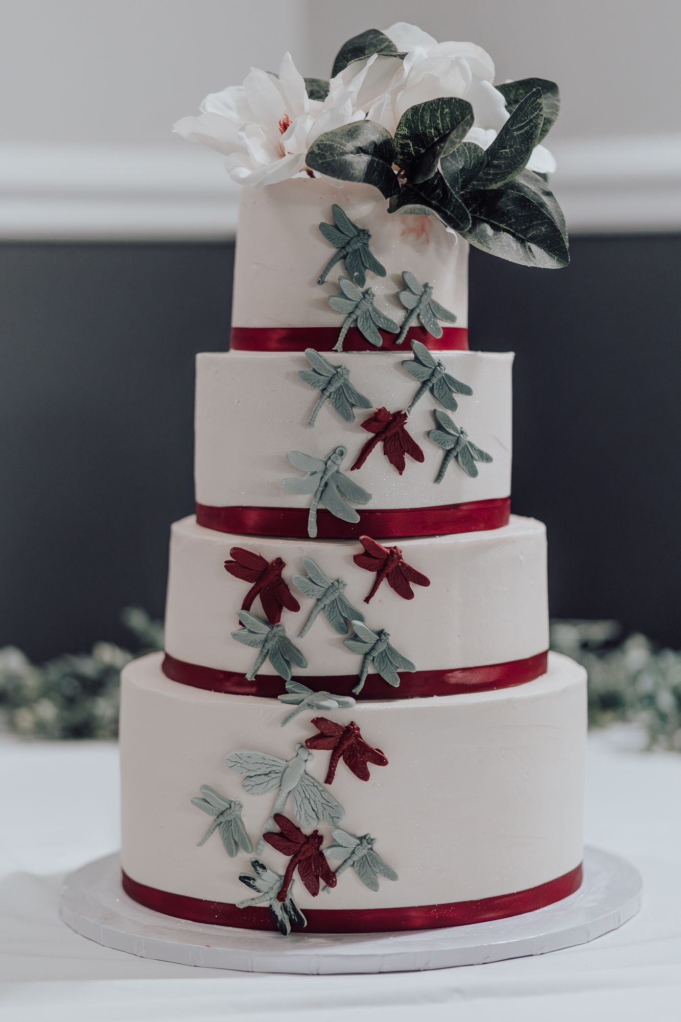 Elegant white wedding cake decorated with burgundy ribbons and sage green foliage.