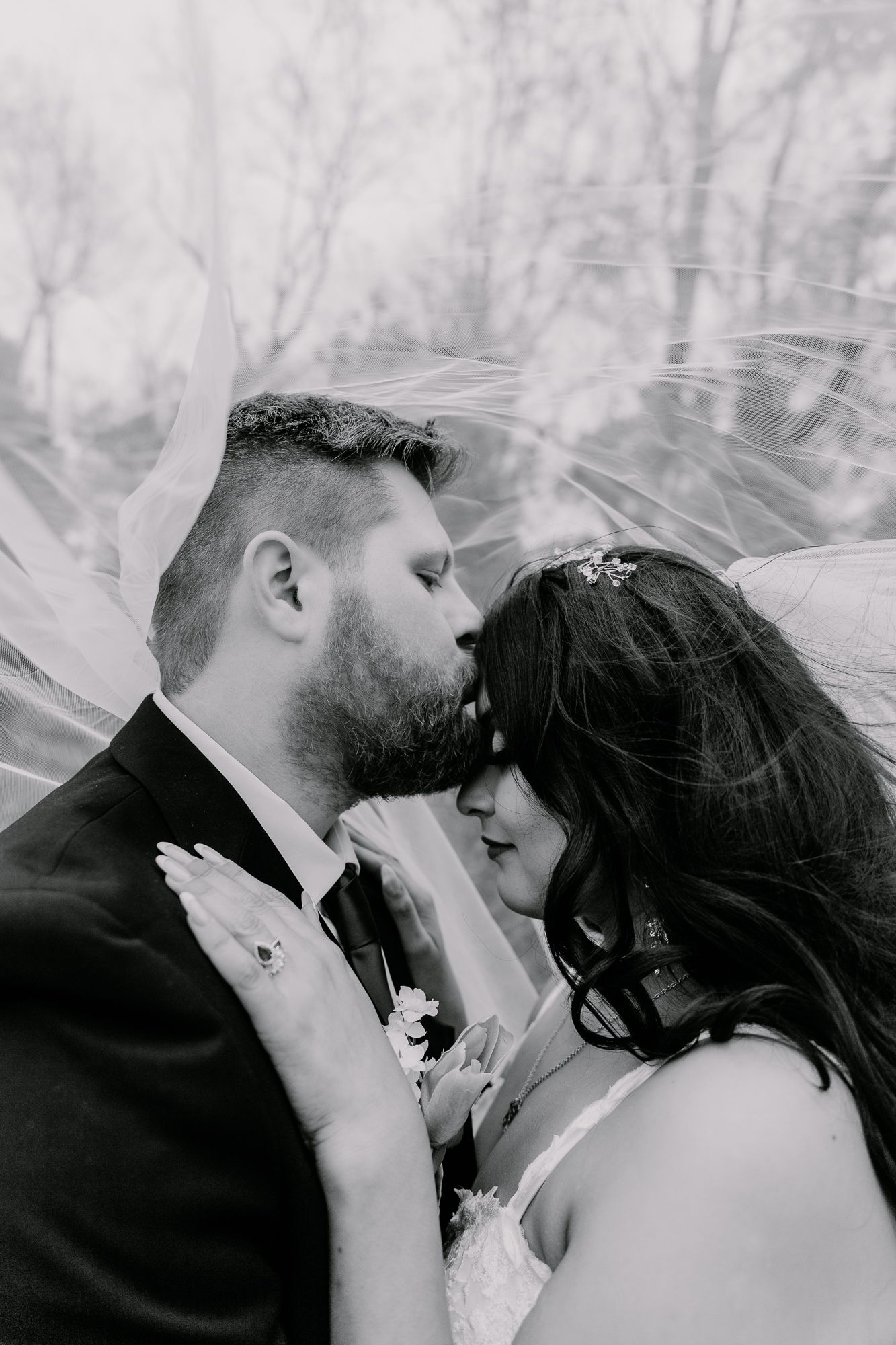 Intimate black and white portrait of newlyweds sharing a tender moment under flowing veil.