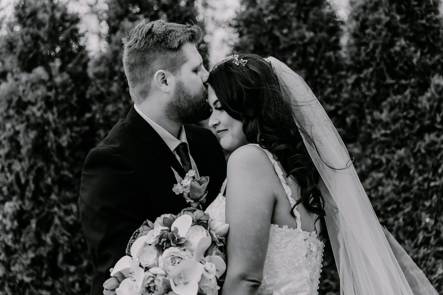 Black and white portrait of newlyweds sharing an intimate moment with wedding bouquet.