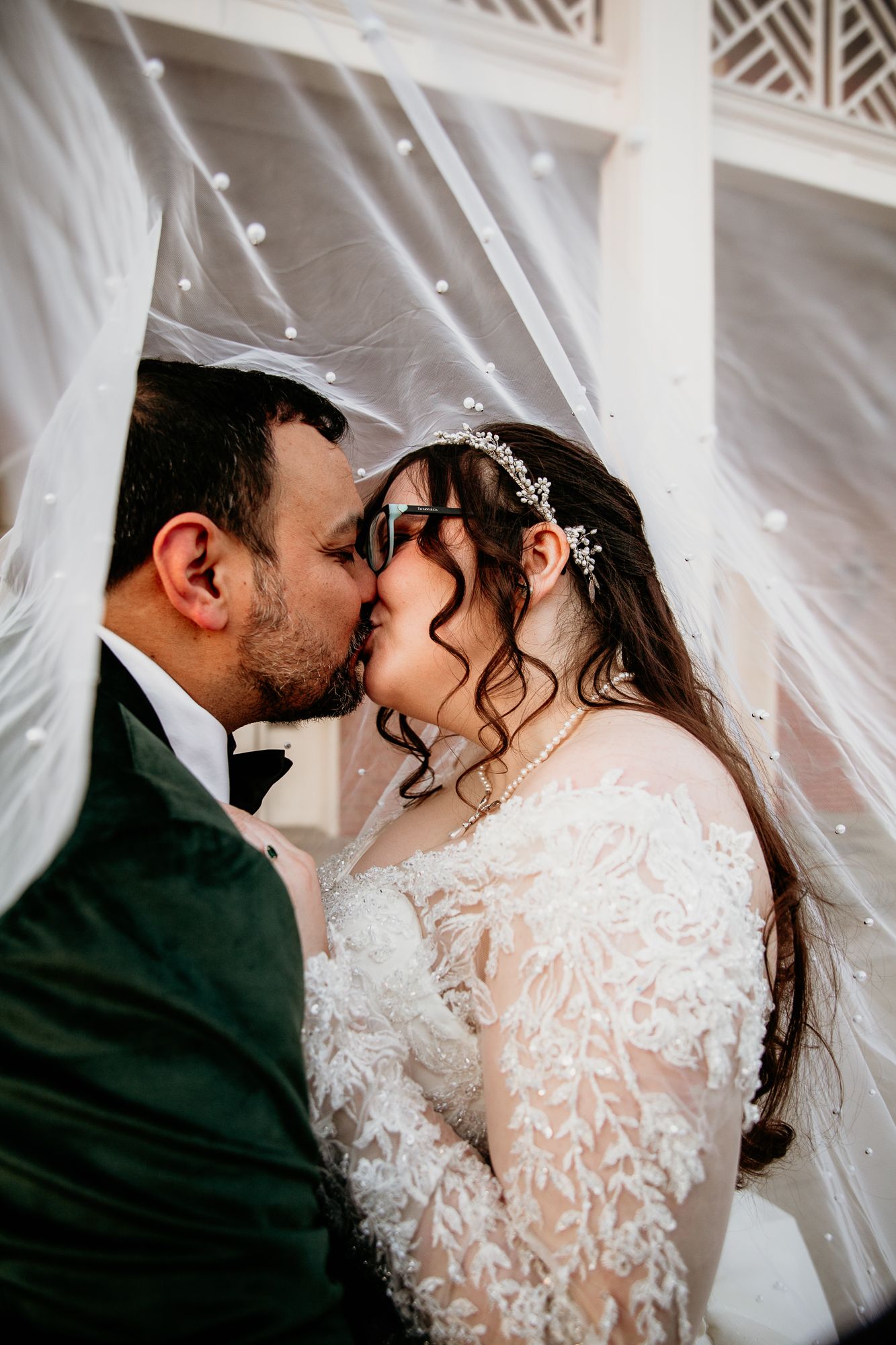 Romantic wedding moment captured through flowing white veil in soft lighting.