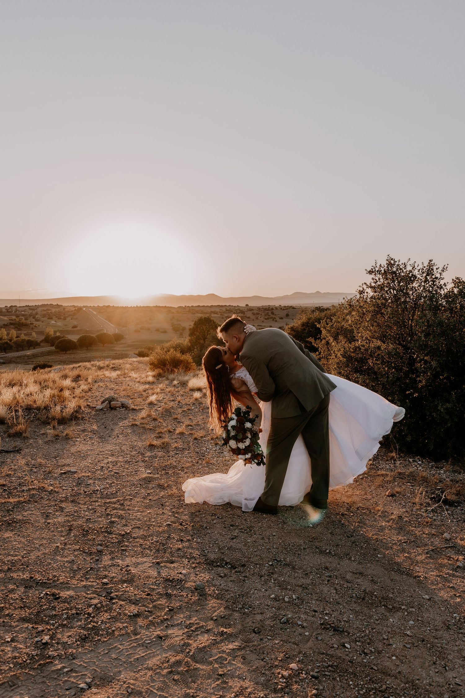 Romantic dip pose by wedding couple on desert mountain during sunset photo session.
