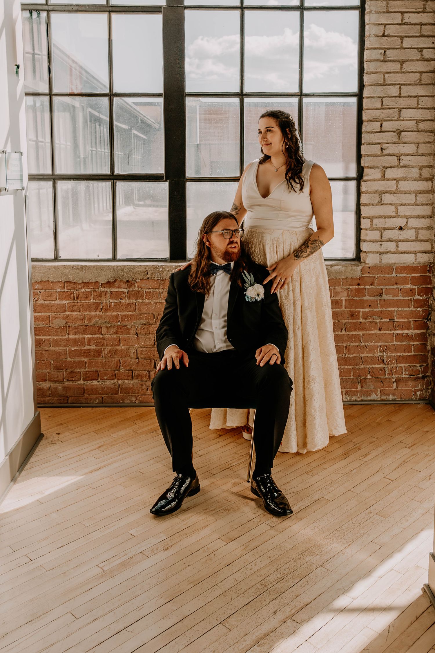 Stylish wedding portrait with groom seated and bride standing in modern industrial space.