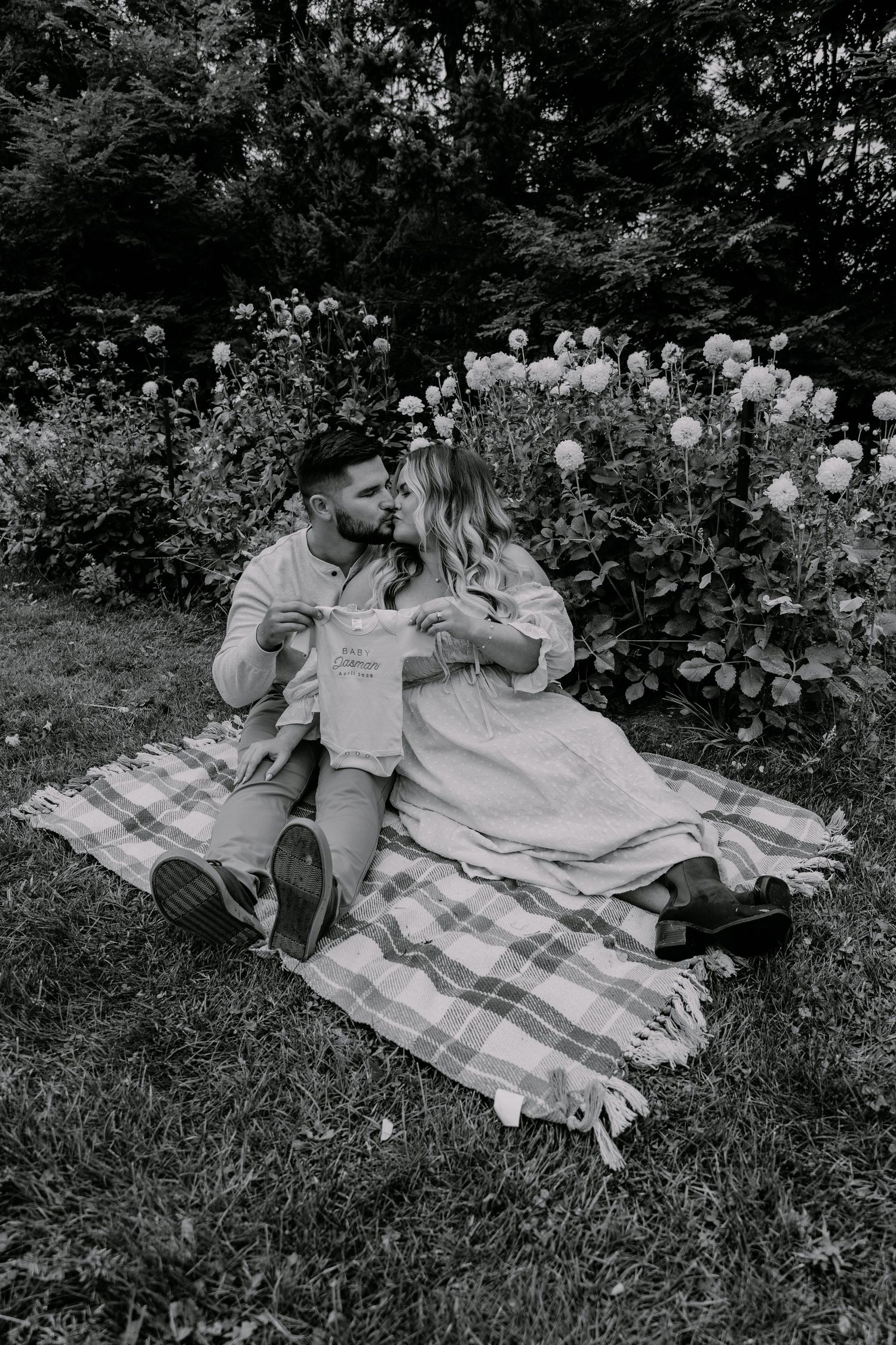 Black and white photo of couple relaxing on picnic blanket in garden setting.