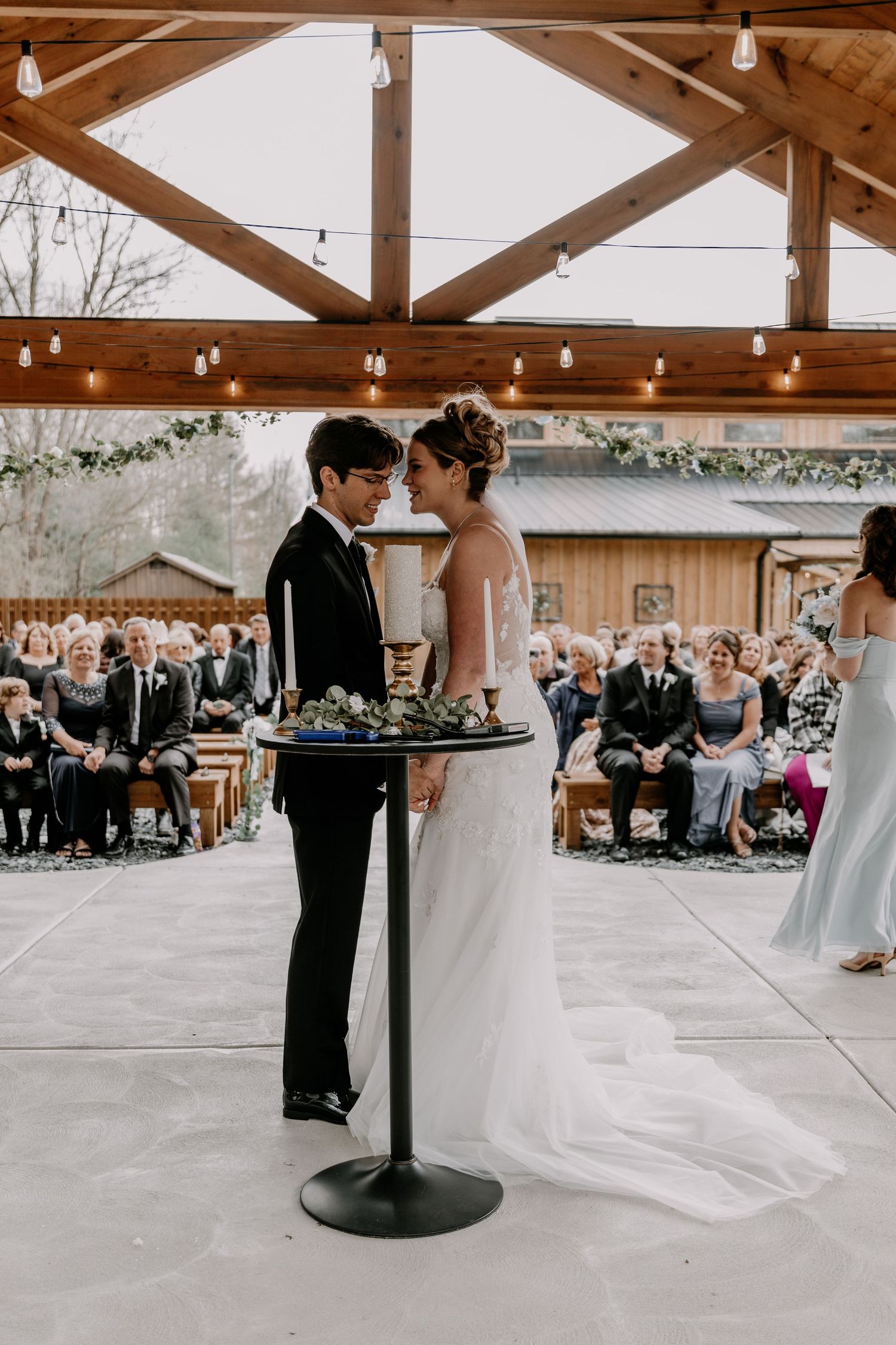 Bride and groom exchanging vows at modern rustic wedding ceremony with guests watching.