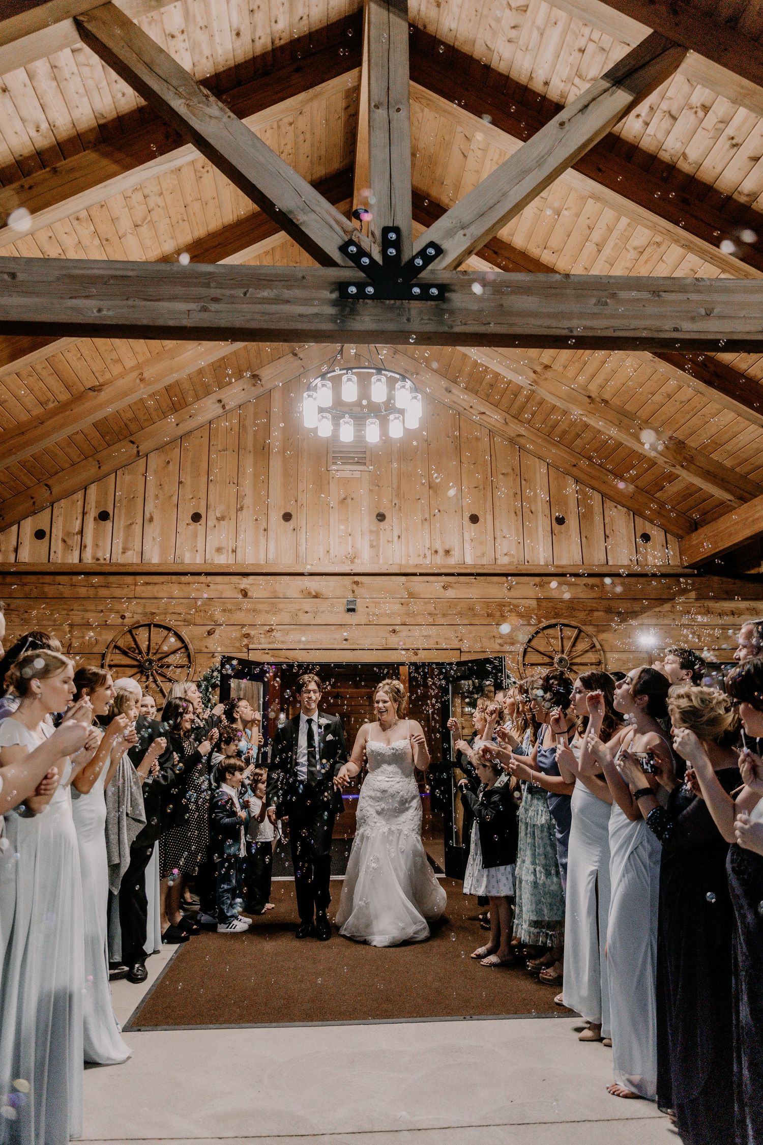 Wide panoramic view of a wedding ceremony in a rustic barn venue with exposed wooden beams.