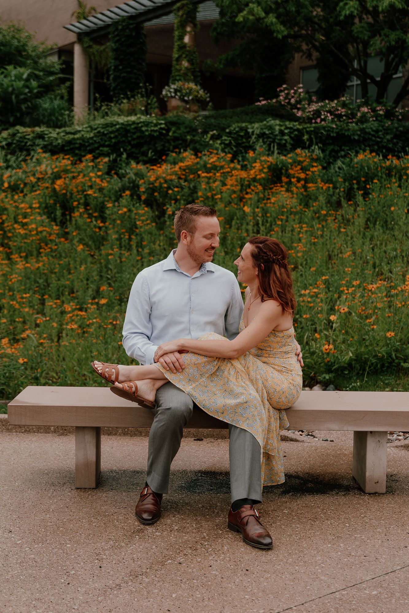 A couple shares a romantic moment on a bench surrounded by blooming orange flowers in a garden.