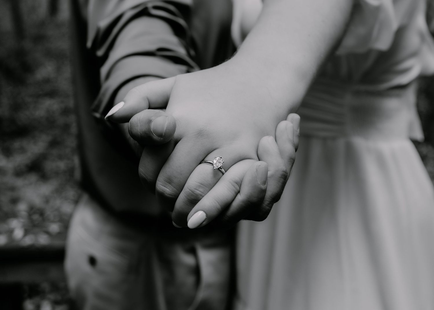 Close-up black and white photo of hands clasped together showing an engagement ring.
